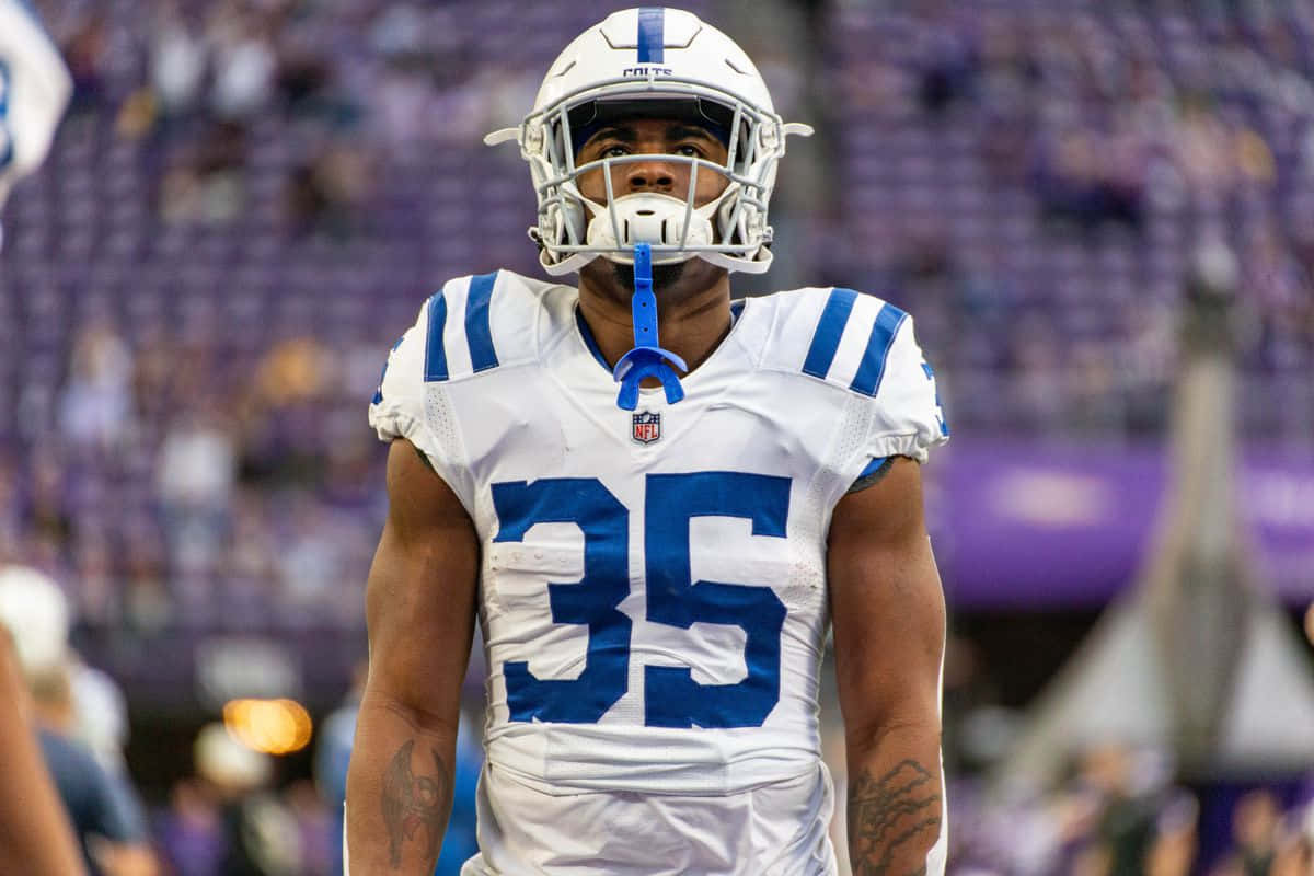  壁紙 — 一名專注的NFL球員身穿白色和藍色球衣，背號35，在體育場燈光下於比賽中站在場上。
