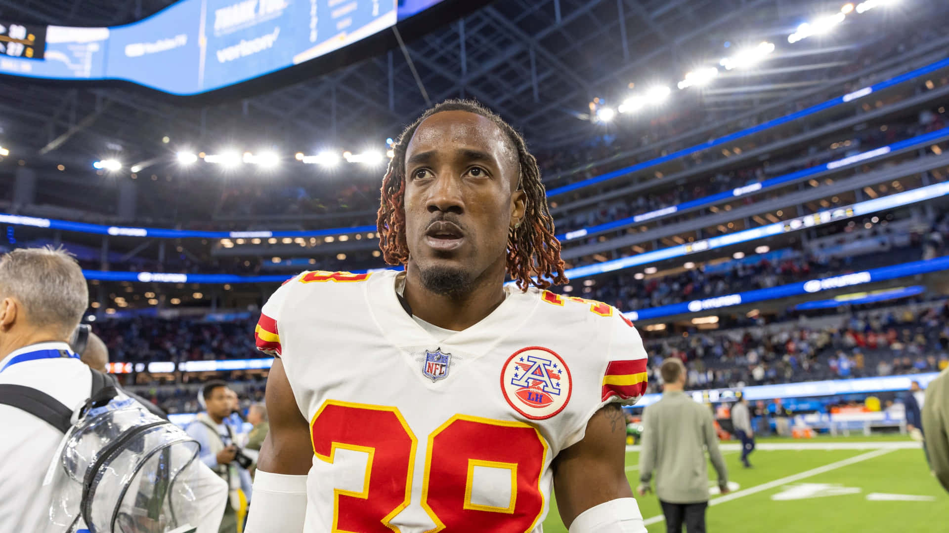  壁紙 — 一名專注的NFL球員身穿白色球衣，紅色20號碼，站在體育場燈光下明亮照明的足球場上。