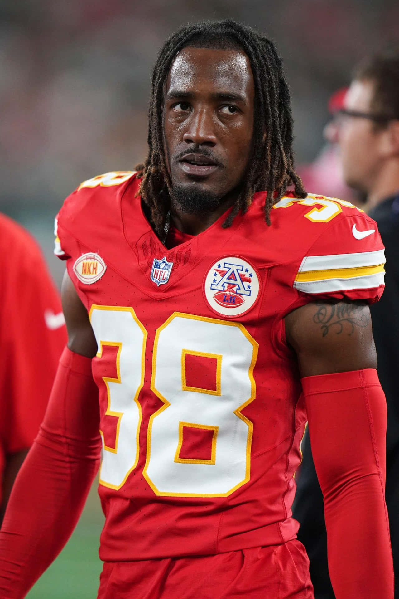  壁紙 — 一名專注的NFL球員身穿紅色38號球衣，在體育場燈光下於比賽中站在場上。