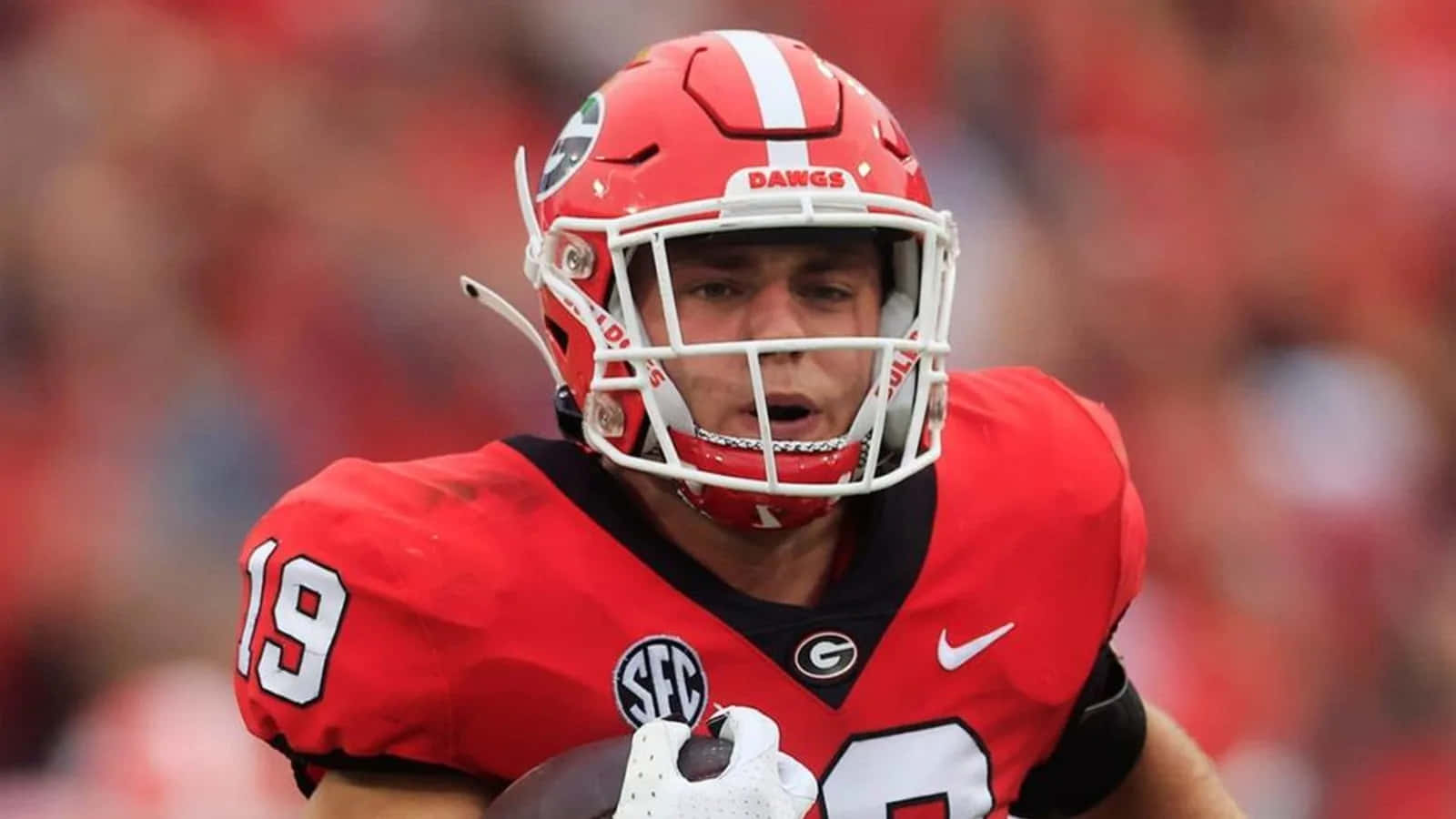  壁紙 — 一名專注的美式足球員身穿紅色Georgia Bulldogs球衣，在日間比賽中帶球奔跑。