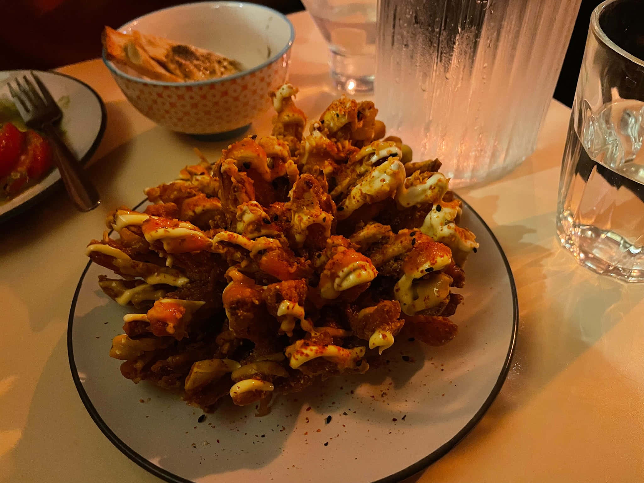 Beautiful Food 桌布 壁紙 — 一盤酥脆炸蟹鉗搭配融化起司和香料，放在溫暖燈光下的桌子上，旁邊有玻璃杯和碗。