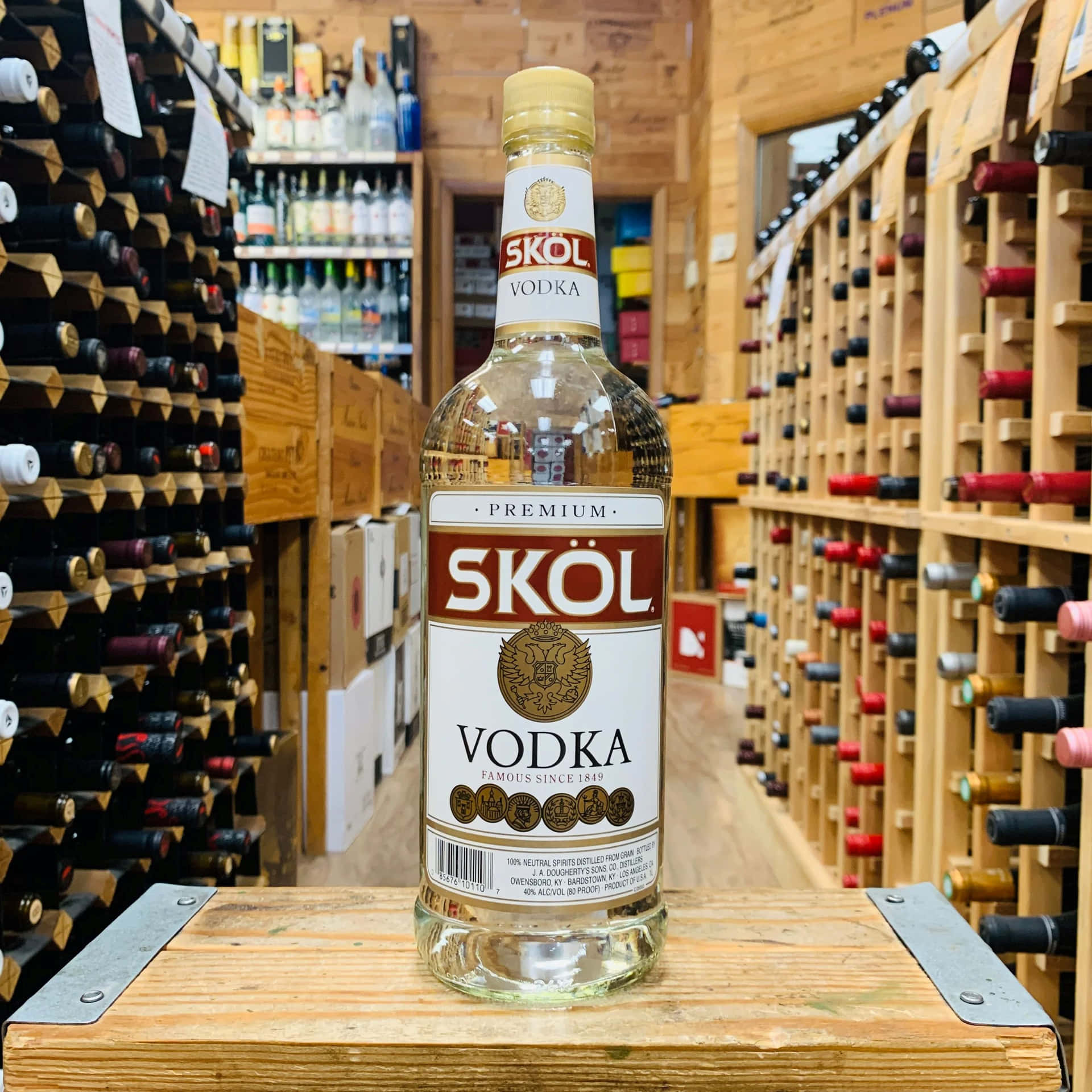  壁紙 — 一瓶透明的Skol Vodka放在木箱中央，位於燈光溫暖的酒舖通道，兩旁是酒架。