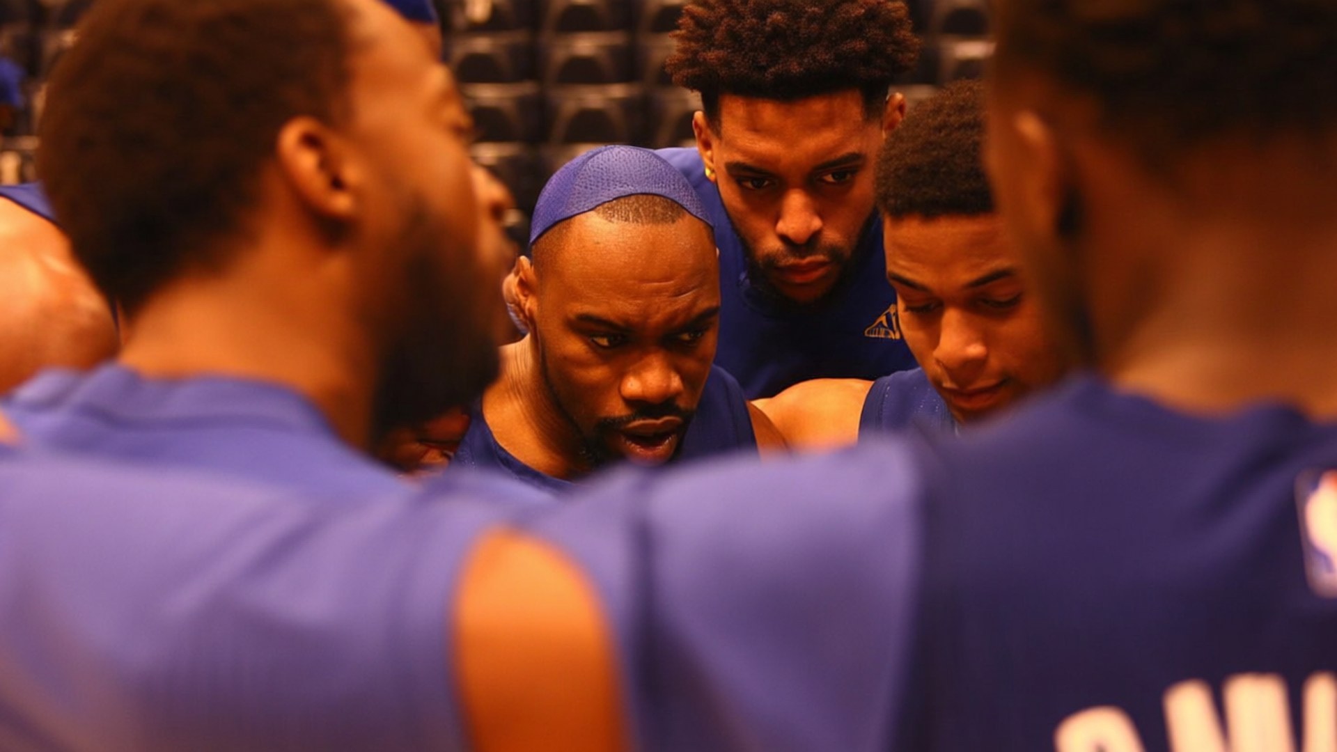 Teammate Huddle Bond 壁紙 — 一群身穿藍色球衣的籃球運動員在球場暫停期間緊密地圍在一起。
