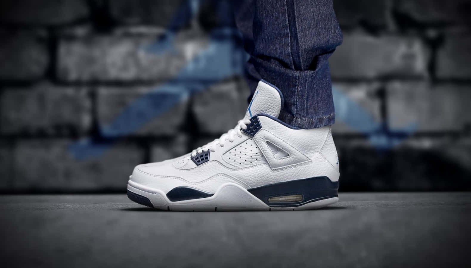 一雙白色和海軍藍色的Air Jordan 4運動鞋在塗鴉磚牆上的特寫。 — Air Jordan 壁紙