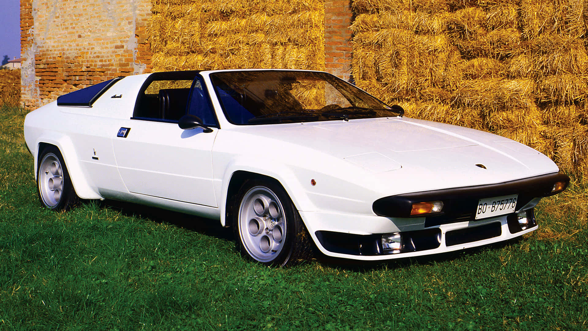 Lamborghini Silhouette 桌布 壁紙 — 一輛純白色的藍寶堅尼 Jalpa 跑車停放在綠色草地上，旁邊有金色乾草捆和磚牆。