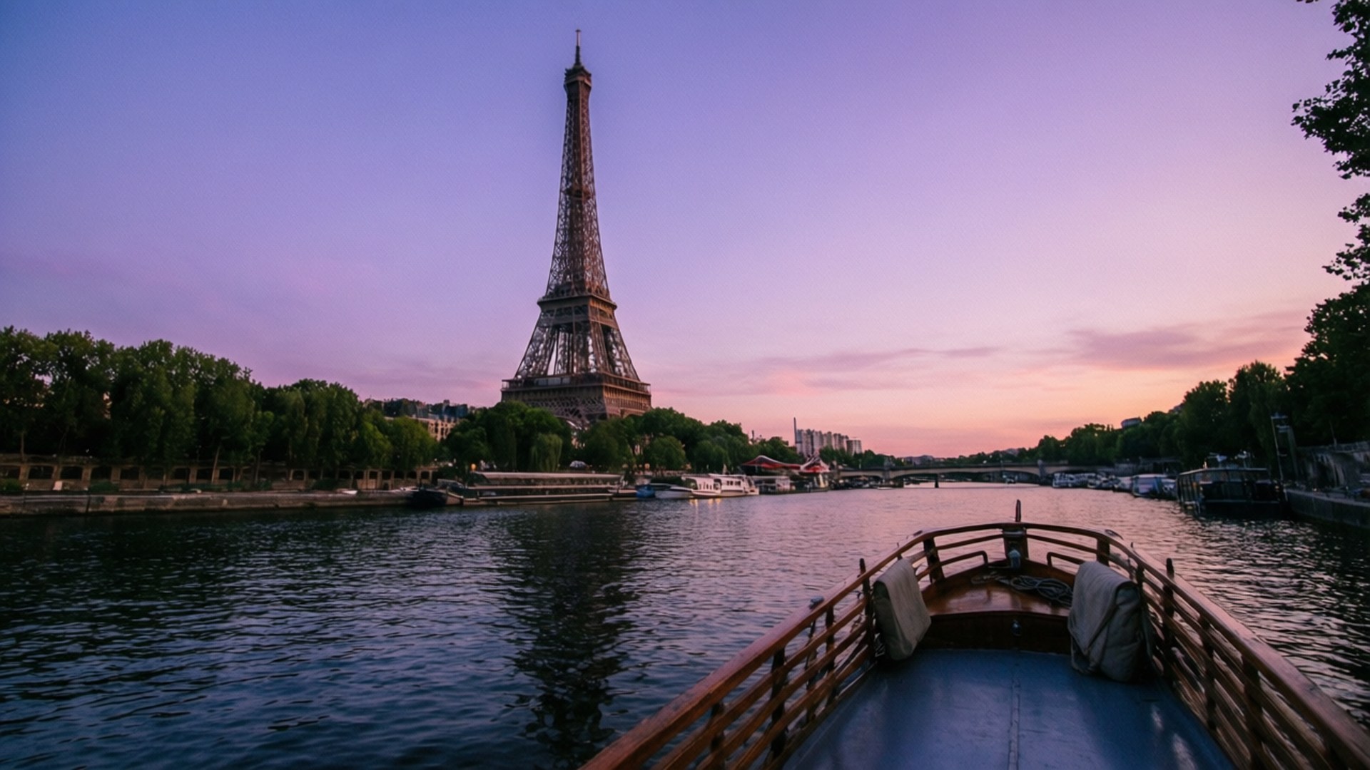 Seine River Reflection 壁紙 — 一艘船在黃昏時沿塞納河航行，艾菲爾鐵塔在紫色和粉紅色的天空襯托下呈現剪影。