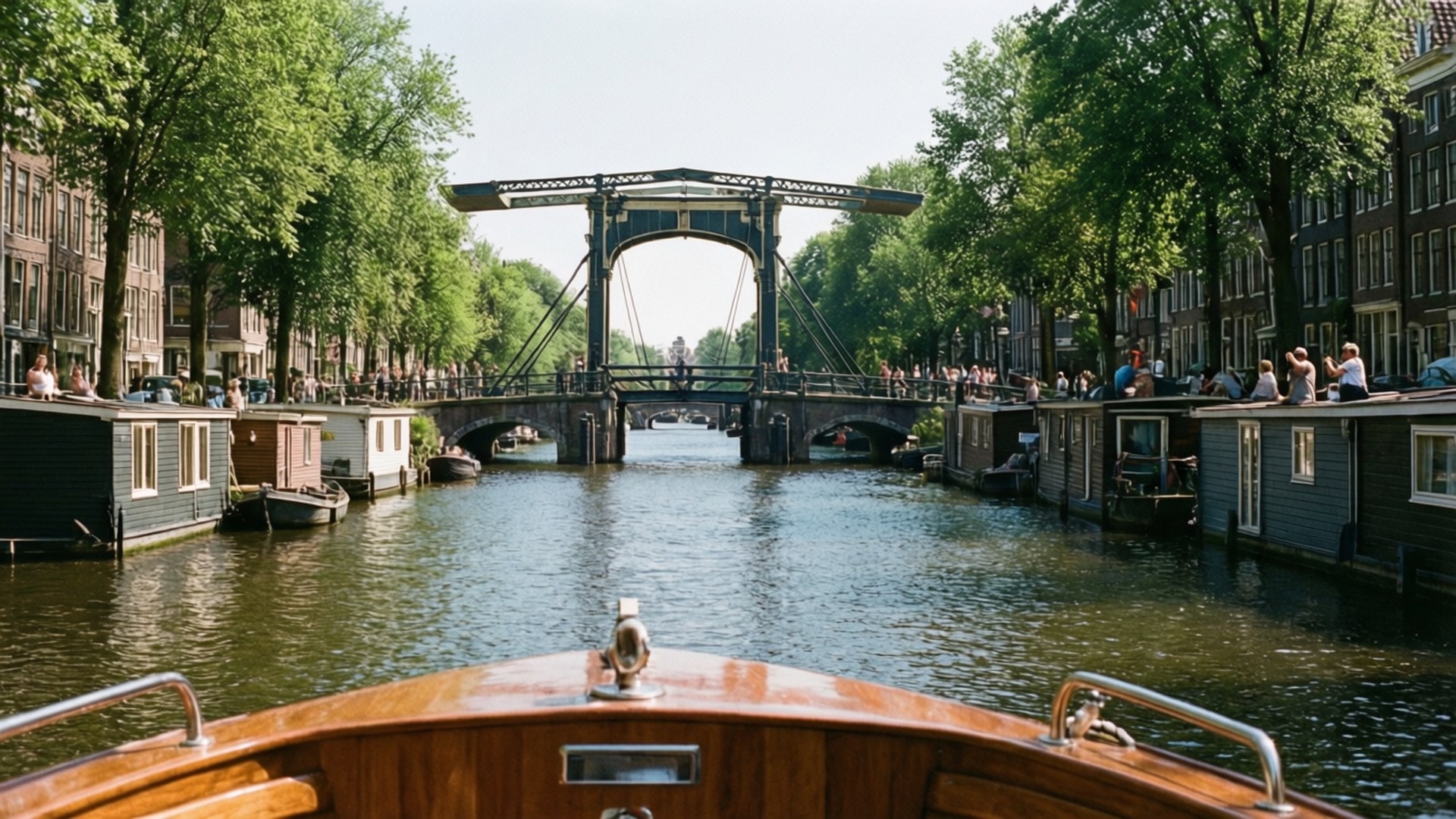 Amsterdam 桌布 壁紙 — 一艘木船在陽光明媚的阿姆斯特丹運河上，在歷史悠久的開合橋下滑行，兩旁是綠樹和運河房屋。