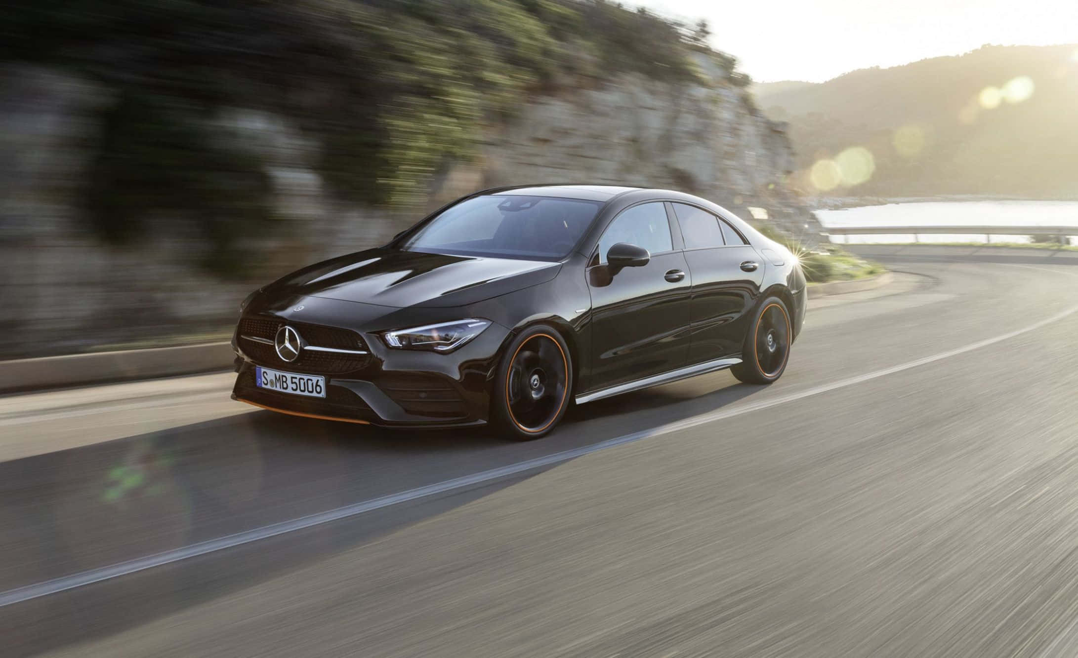 Mercedes Benz Cla-class 桌布 壁紙 — 一台流線型的黑色Mercedes-AMG CLA 35 S E Performance在模糊的綠意和陽光照射下，沿著蜿蜒的海岸道路飛馳。
