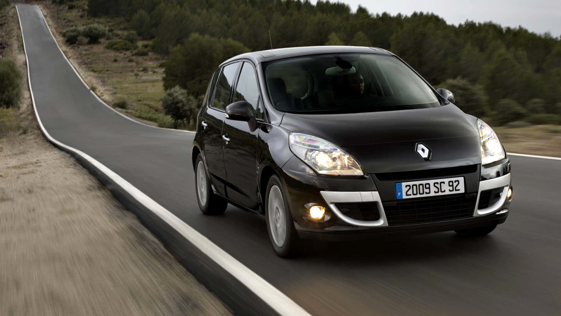 Renault Scenic 桌布 壁紙 — 一台時尚的黑色雷諾 Scenic 沿著蜿蜒的鄉村道路穿過森林景觀行駛。