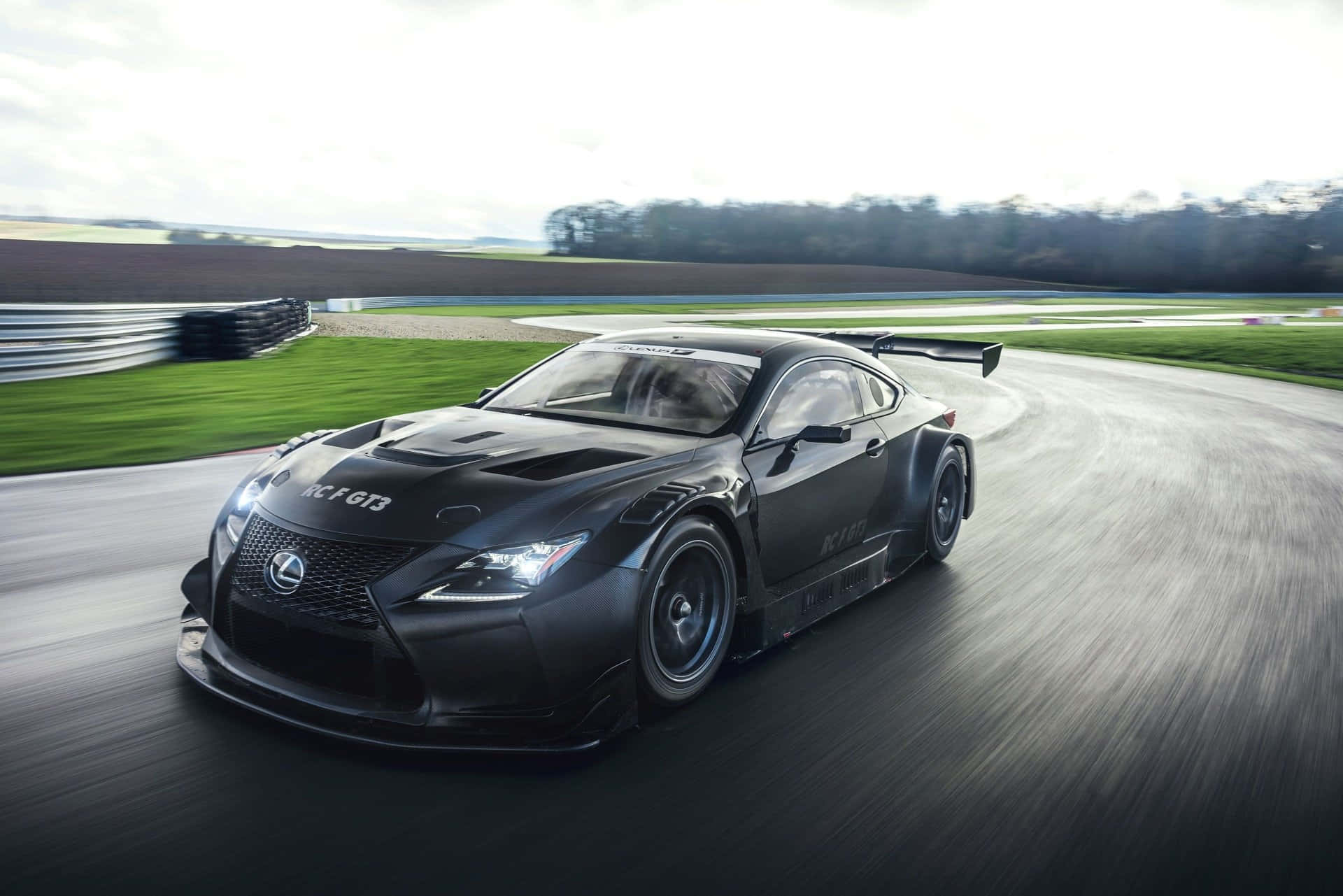 Lexus Rc F 桌布 壁紙 — 一台時尚的黑色 Lexus RC F GT3 賽車在彎曲的賽道上疾馳，帶有動態模糊和綠色草地環境。