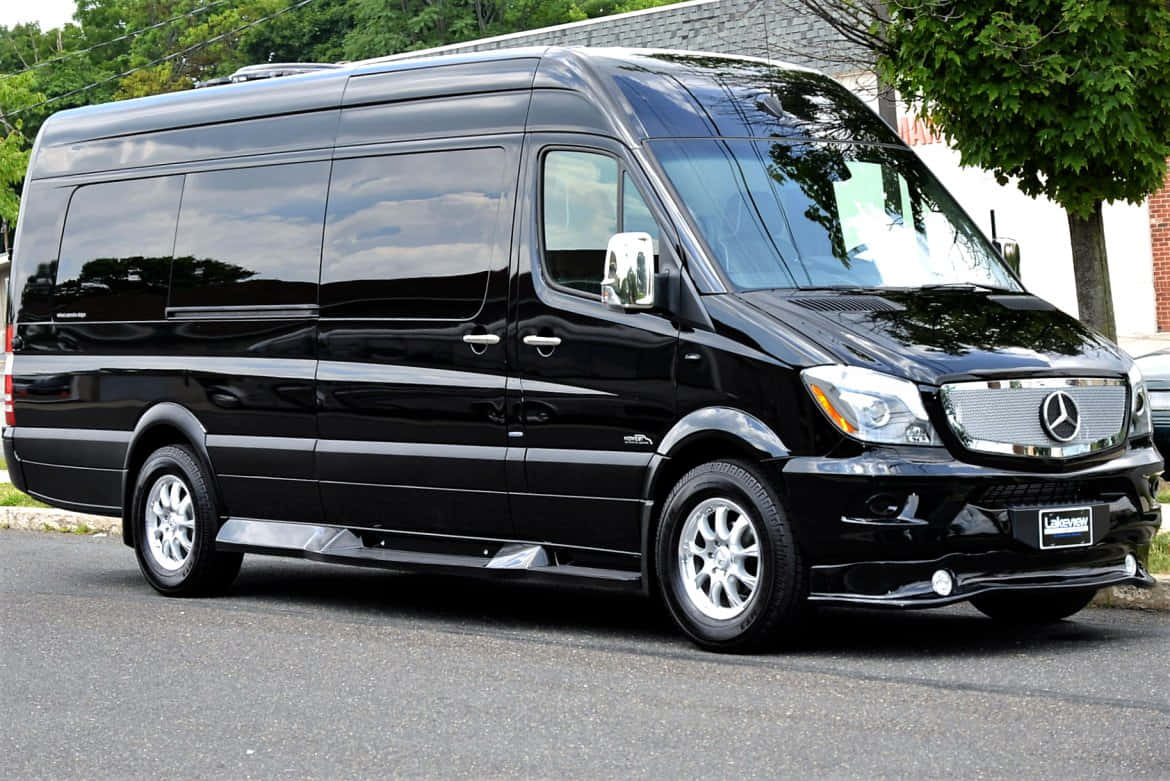 Mercedes Benz Sprinter 桌布 壁紙 — 一台時尚的黑色 Mercedes-Benz Sprinter 廂型車停在柏油路上，背景有樹木和磚造建築。
