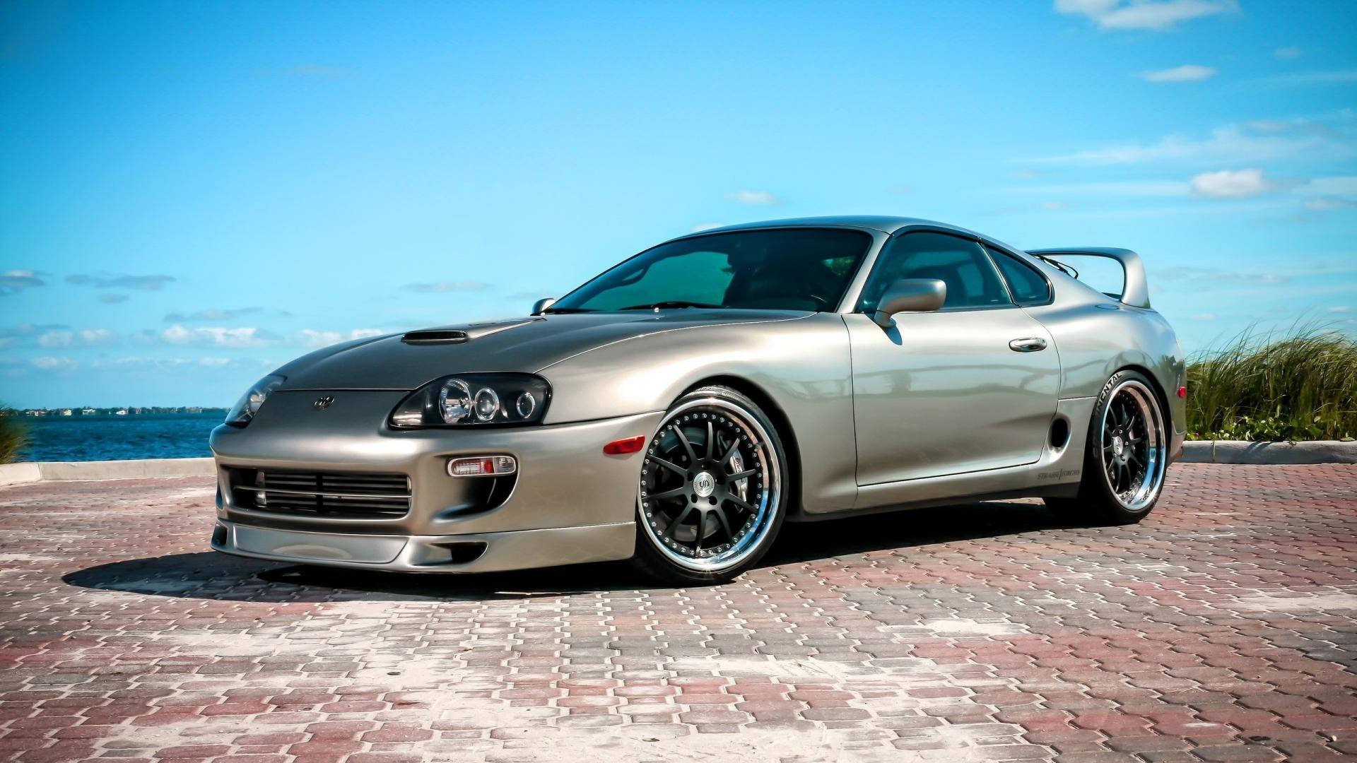 銀色豐田Supra跑車停泊在近海的紅磚碼頭上，日落時分。 — Toyota Supra 壁紙