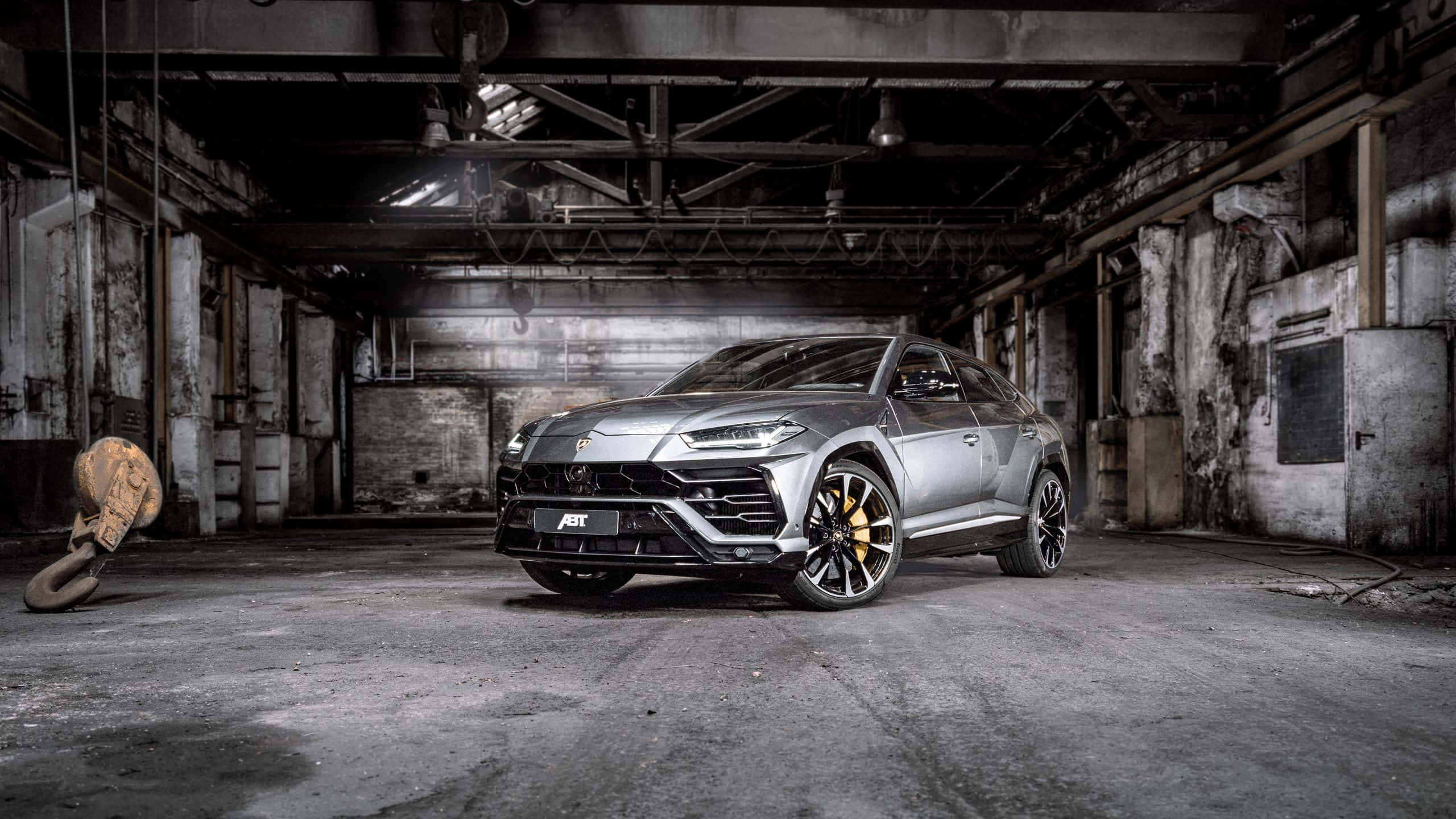 Lamborghini Urus 桌布 壁紙 — 一台時尚的銀色藍寶堅尼 Urus 大膽地停放在一個骯髒的廢棄工業倉庫中，倉庫內有裸露的橫樑和混凝土牆。