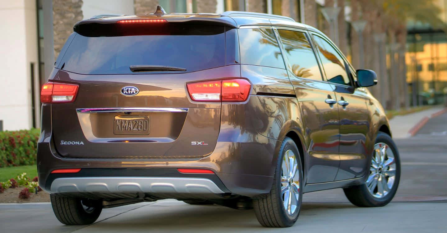 Kia Sedona 桌布 壁紙 — 一台時尚的棕色Kia Sedona小型貨車停放在陽光明媚的街道上，背景有棕櫚樹和建築物。