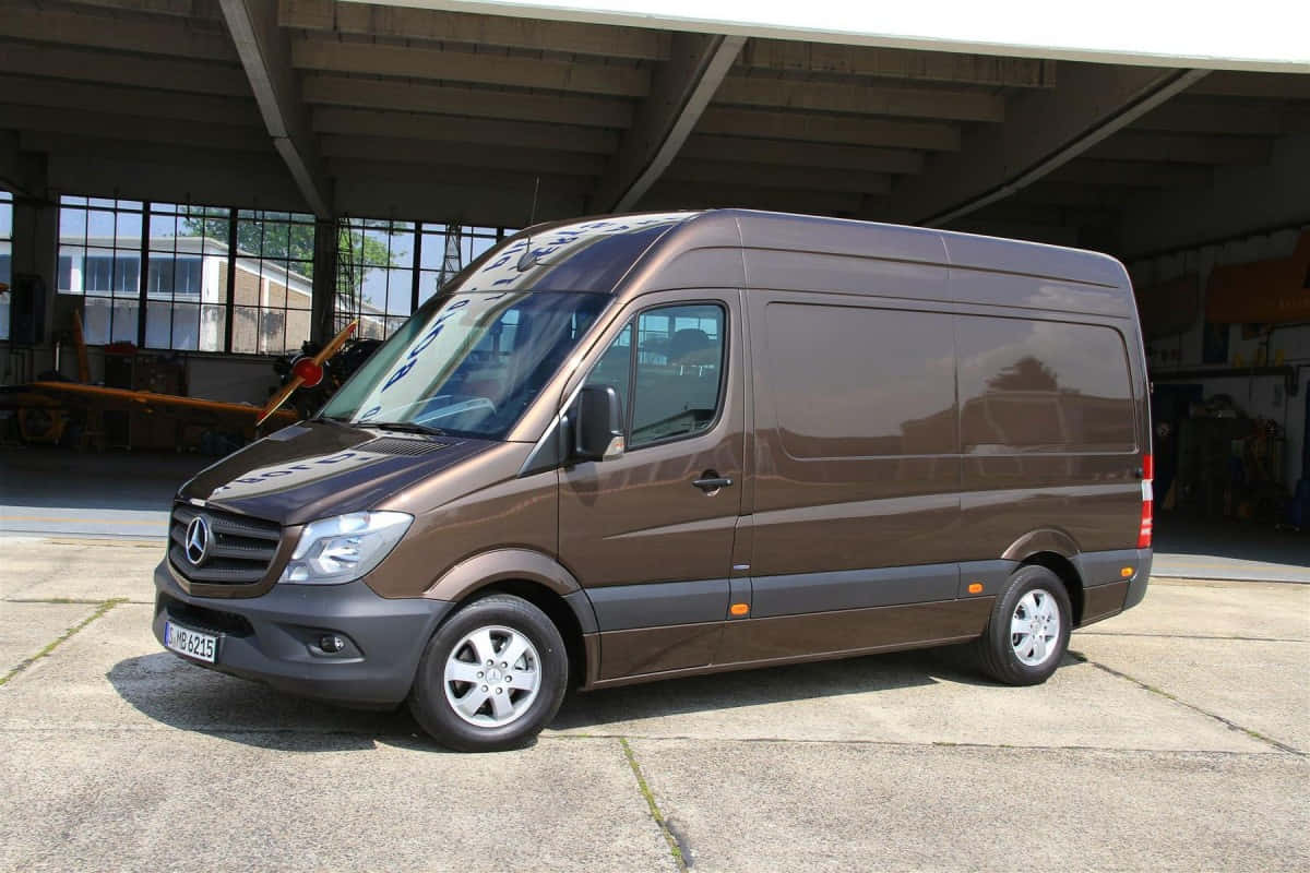 Mercedes Benz Sprinter 桌布 壁紙 — 一台時尚的棕色 Mercedes-Benz Sprinter 客貨車停放在大型工業機庫下，陽光透過窗戶照射進來。