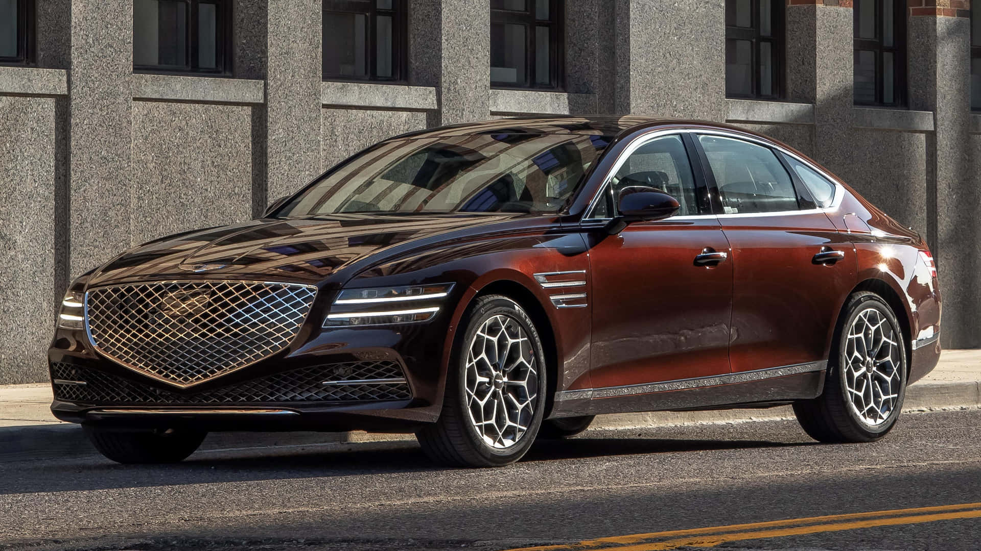 Genesis G80 桌布 壁紙 — 一台時尚的酒紅色Genesis G90轎車在明亮的陽光下閃閃發光，停放在灰色石建築旁的街道上。