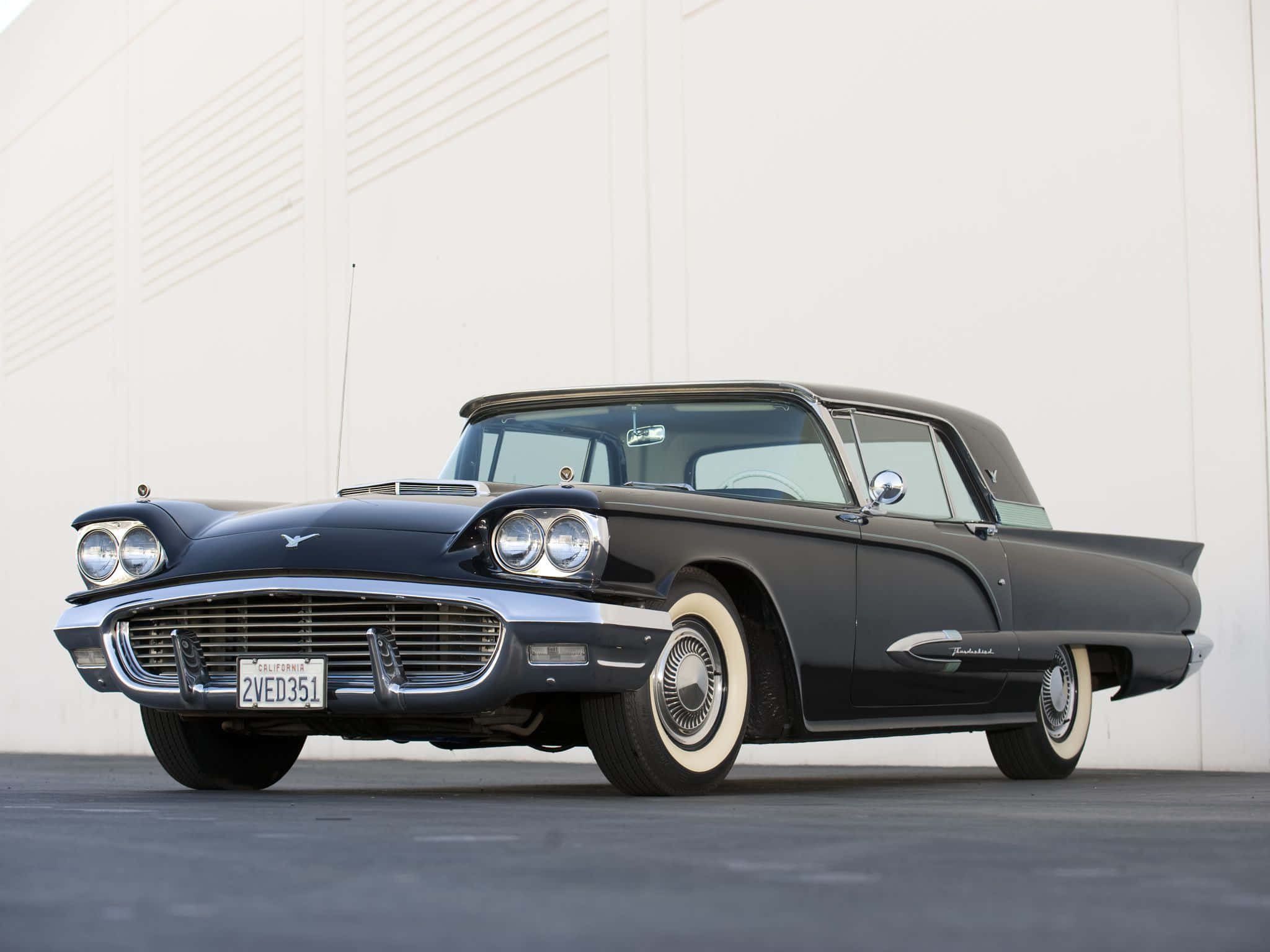 Ford Thunderbird 桌布 壁紙 — 一台時尚的黑色1957年福特雷鳥經典車，配備白邊輪胎，停放在簡約的白色牆壁前。