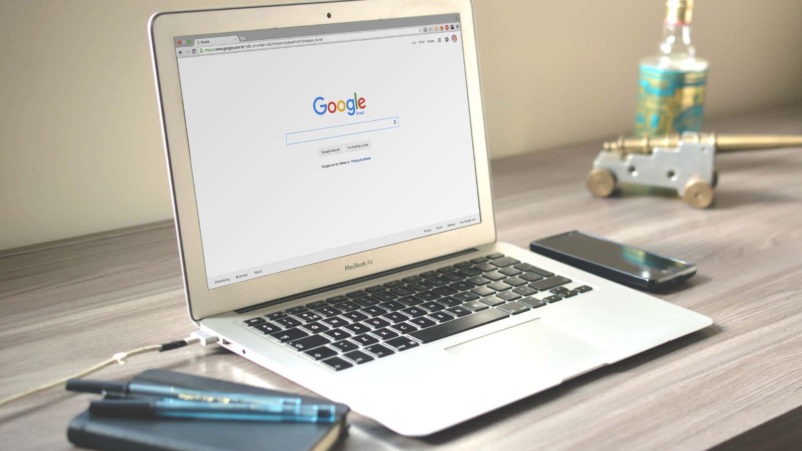木桌上的銀色筆記型電腦，旁邊有電話筆和裝飾瓶。 — Google 壁紙