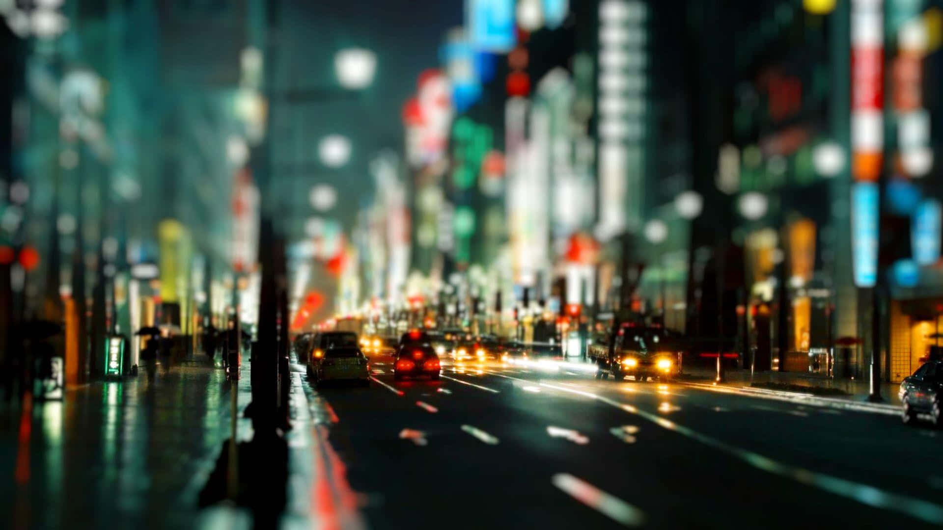  壁紙 — 一條模糊的夜間城市街道，帶有發光的霓虹燈和流動的車頭燈，在潮濕的人行道上反射。