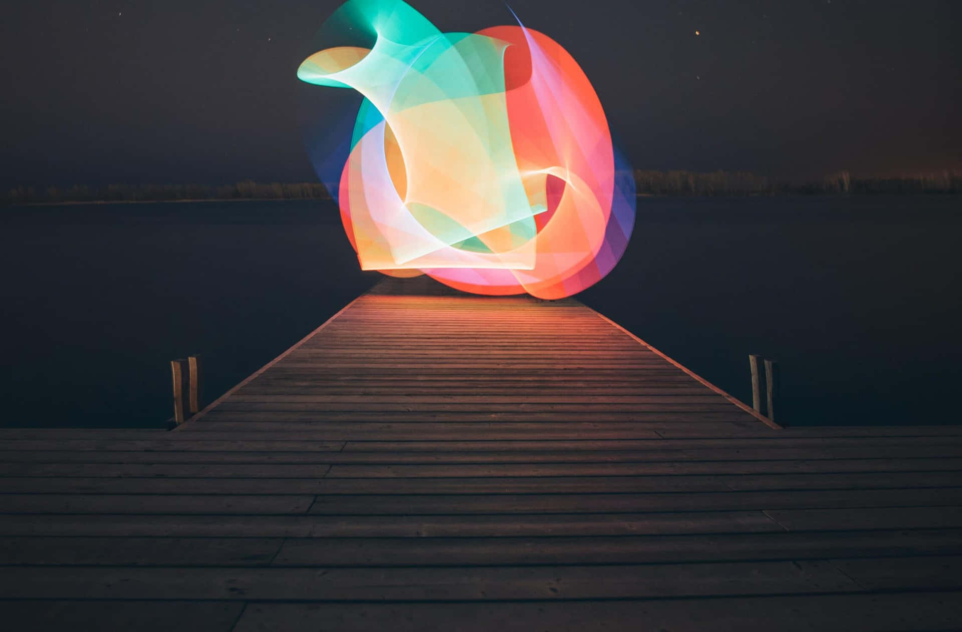  壁紙 — 一條木製碼頭在夜間延伸至黑暗的水面，朝向一個發光的抽象燈光雕塑。