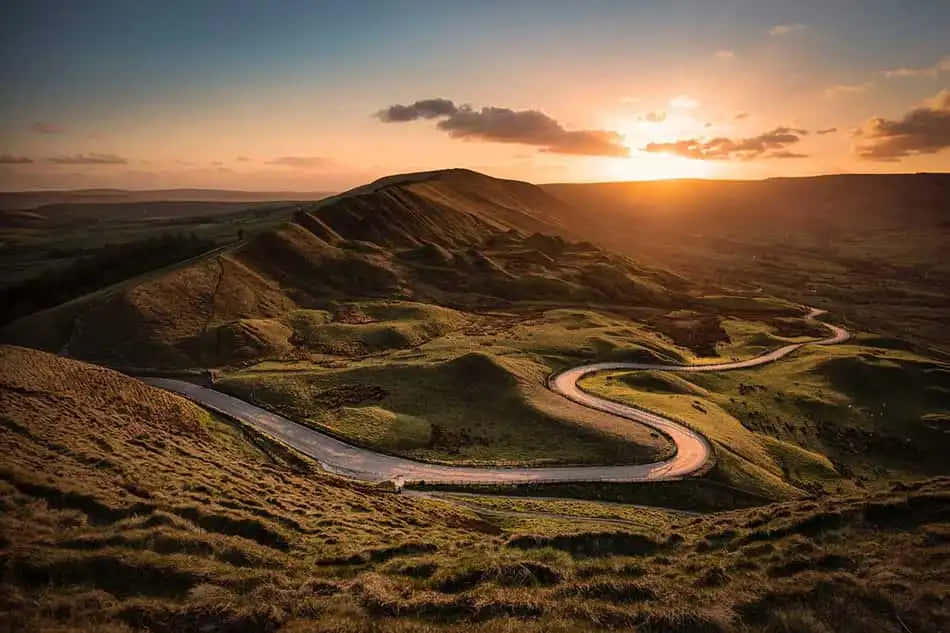 夕陽下蜿蜒穿過起伏綠色山丘的道路 — Google 壁紙