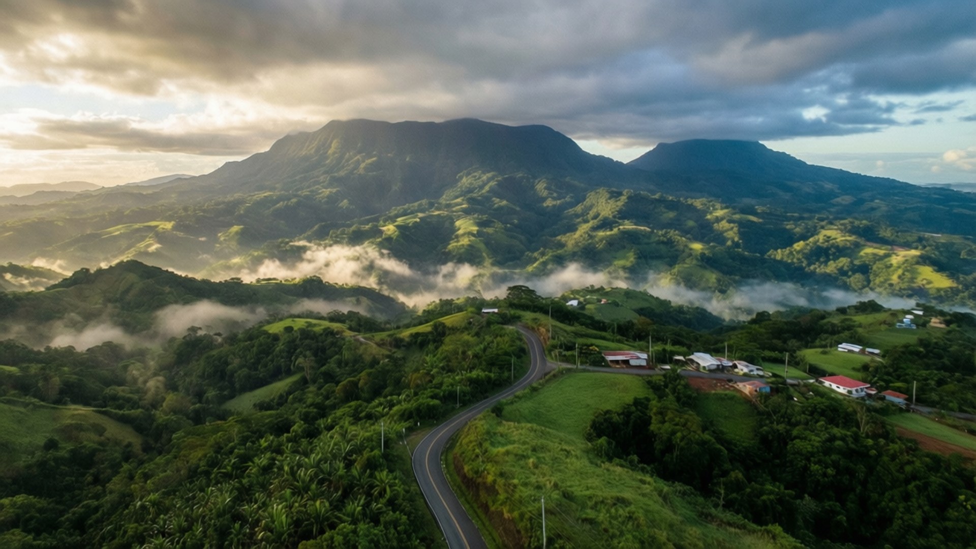 Central Mountain Panorama 壁紙 — 一條蜿蜒的道路蜿蜒穿過鬱鬱蔥蔥的綠色山丘，黎明時分，霧氣籠罩著高聳山脈下的山谷。