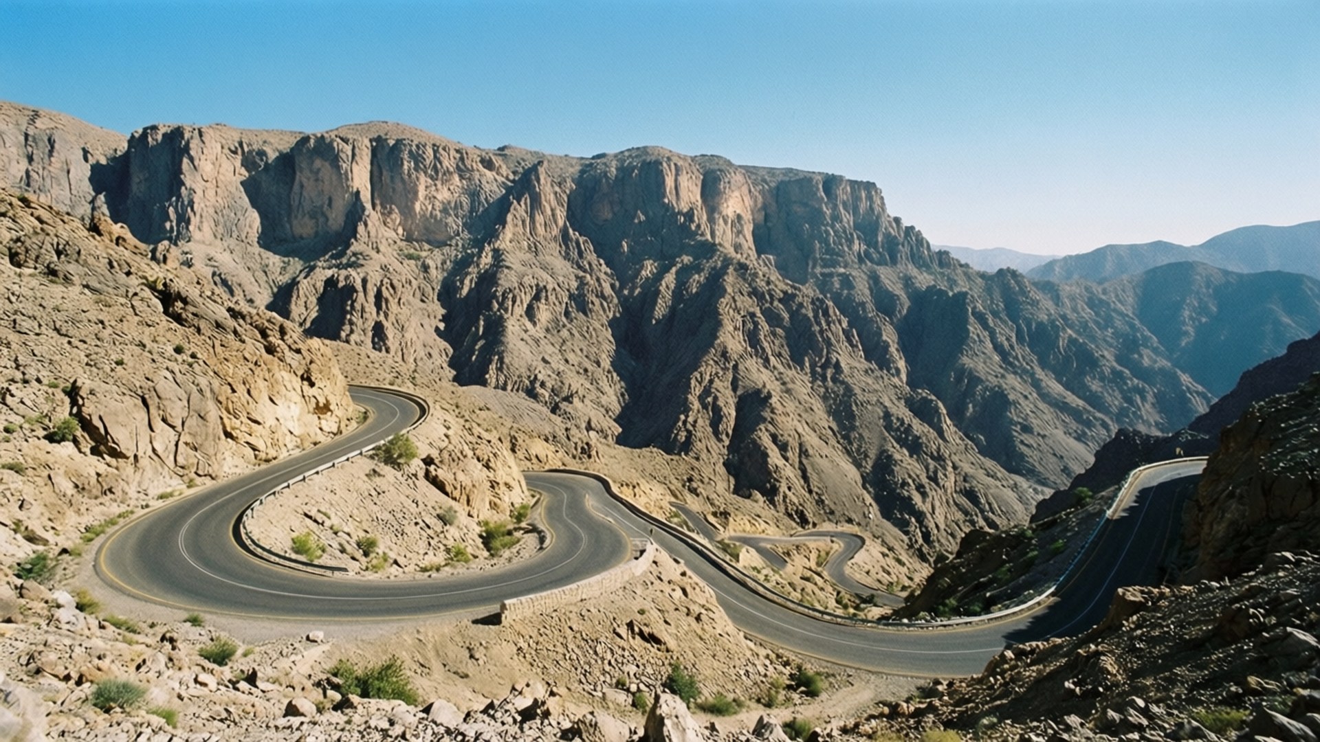 Jebel Jais Mountain Road 壁紙 — 一條蜿蜒的瀝青公路在晴朗的藍天下蜿蜒穿過崎嶇的岩石山脈。