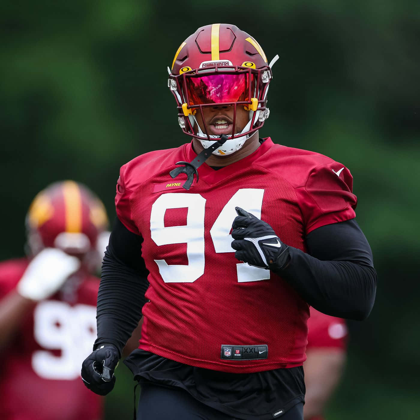  壁紙 — 一位身穿紅色94號球衣、專注的NFL球員，在訓練中戴著反光粉紅色面罩，表情堅定地衝刺。