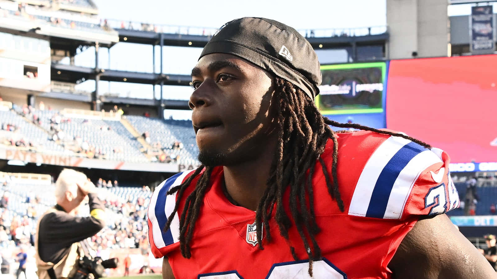  壁紙 — 一位身穿紅色球衣、留著辮子的專注NFL美式足球員，在陽光明媚的球場上凝視前方。