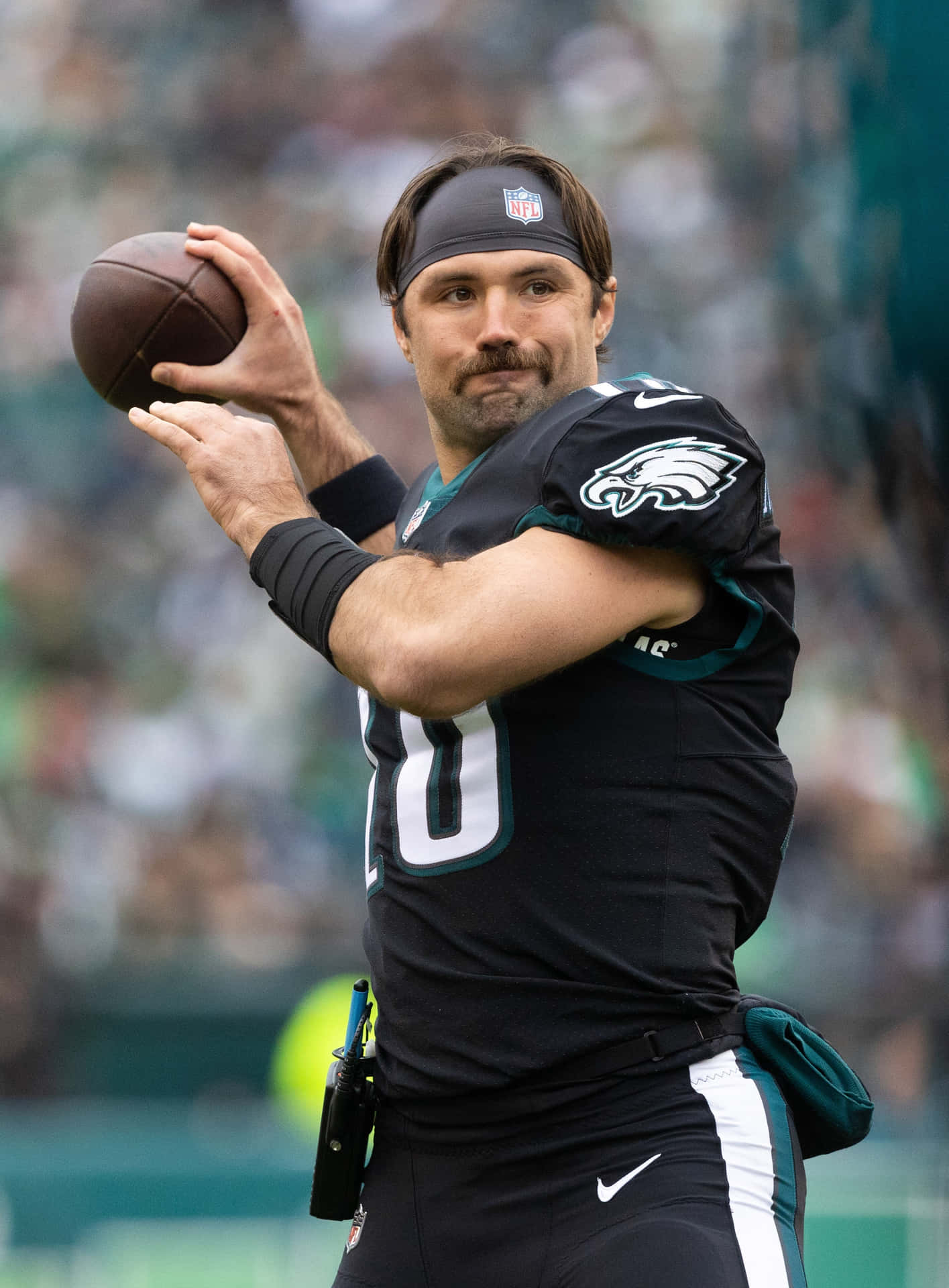  壁紙 — 一位身穿老鷹隊球衣、專注的NFL四分衛在日間比賽中準備擲出橄欖球，背景是模糊的體育場人群。
