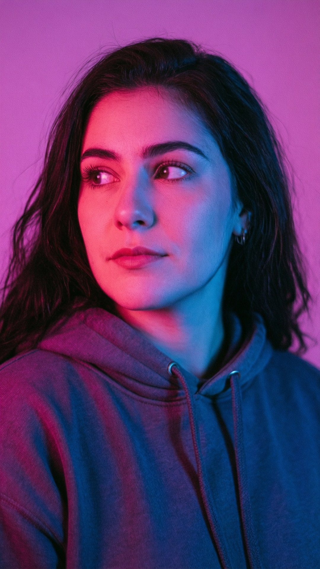 Avani Gregg Aesthetic Glow 壁紙 — 一位穿著連帽衫的年輕女子在充滿活力的粉紅色和藍色霓虹燈光下若有所思地側視。