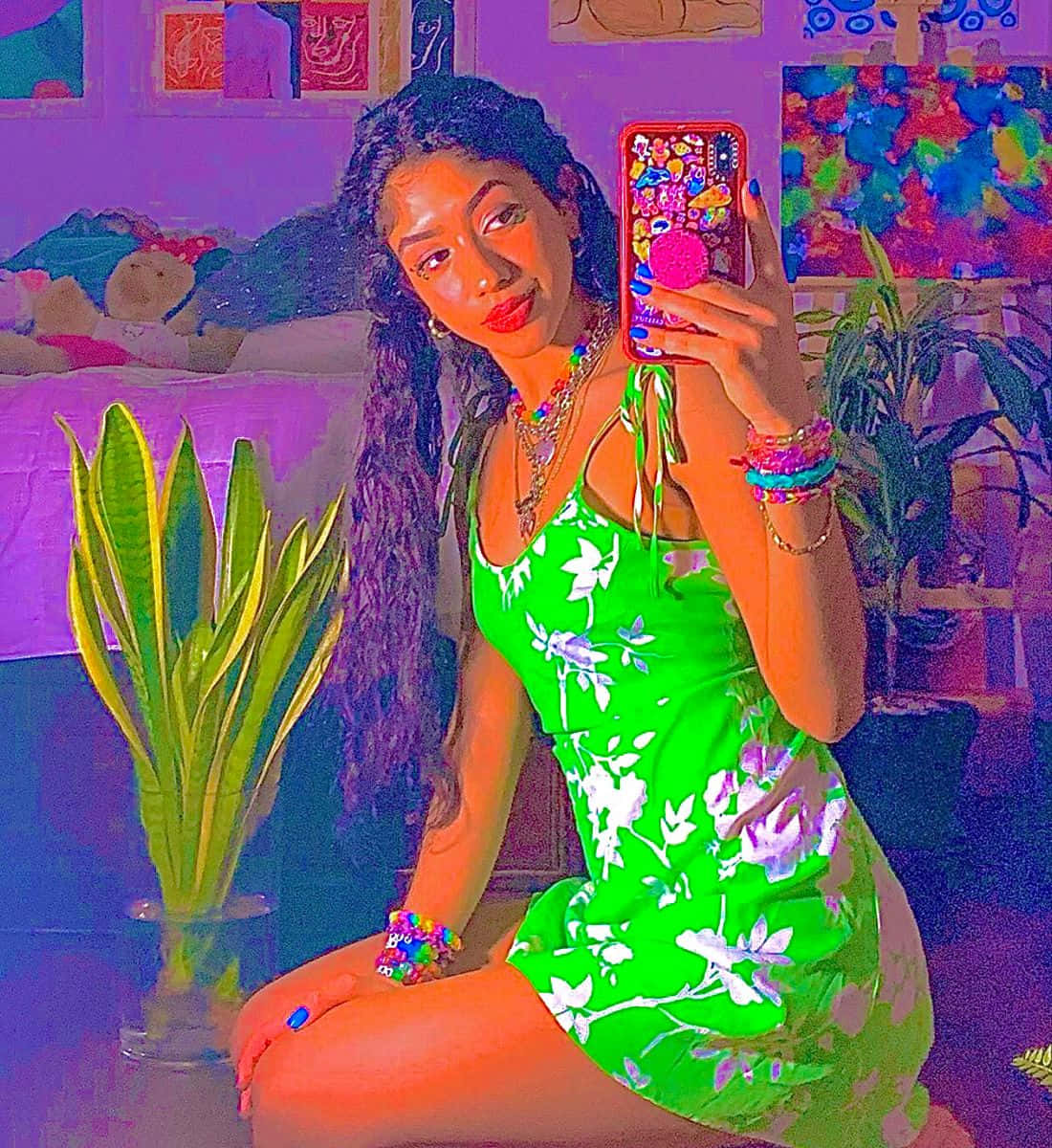  壁紙 — 一位穿著螢光綠色花卉連衣裙的年輕女性在一個充滿植物和藝術品的色彩繽紛的臥室裡自拍。
