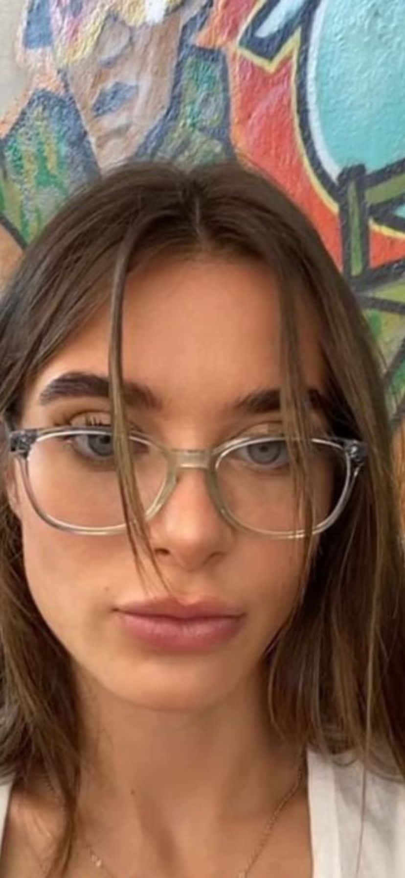  壁紙 — 一位戴眼鏡、棕色頭髮的年輕女性在色彩繽紛的塗鴉牆前直視鏡頭。