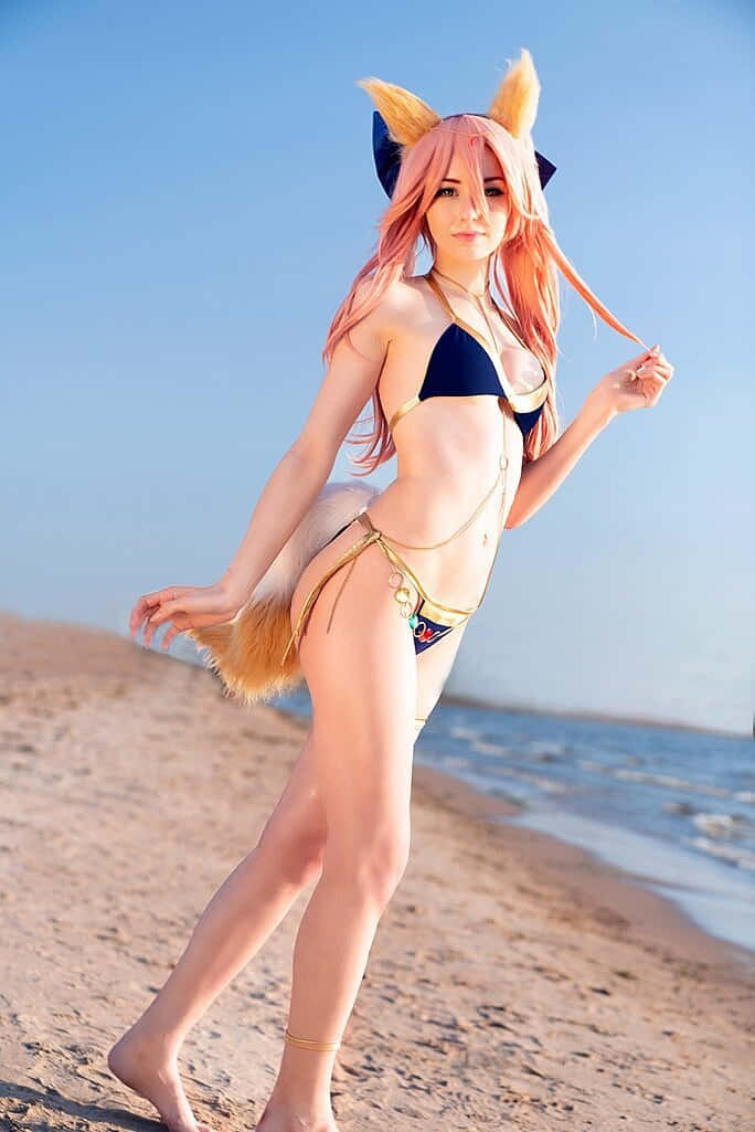  壁紙 — 一位戴著狐狸耳朵和尾巴的cosplayer在陽光明媚的海灘上穿著藍色和金色的比基尼優雅地擺姿勢。