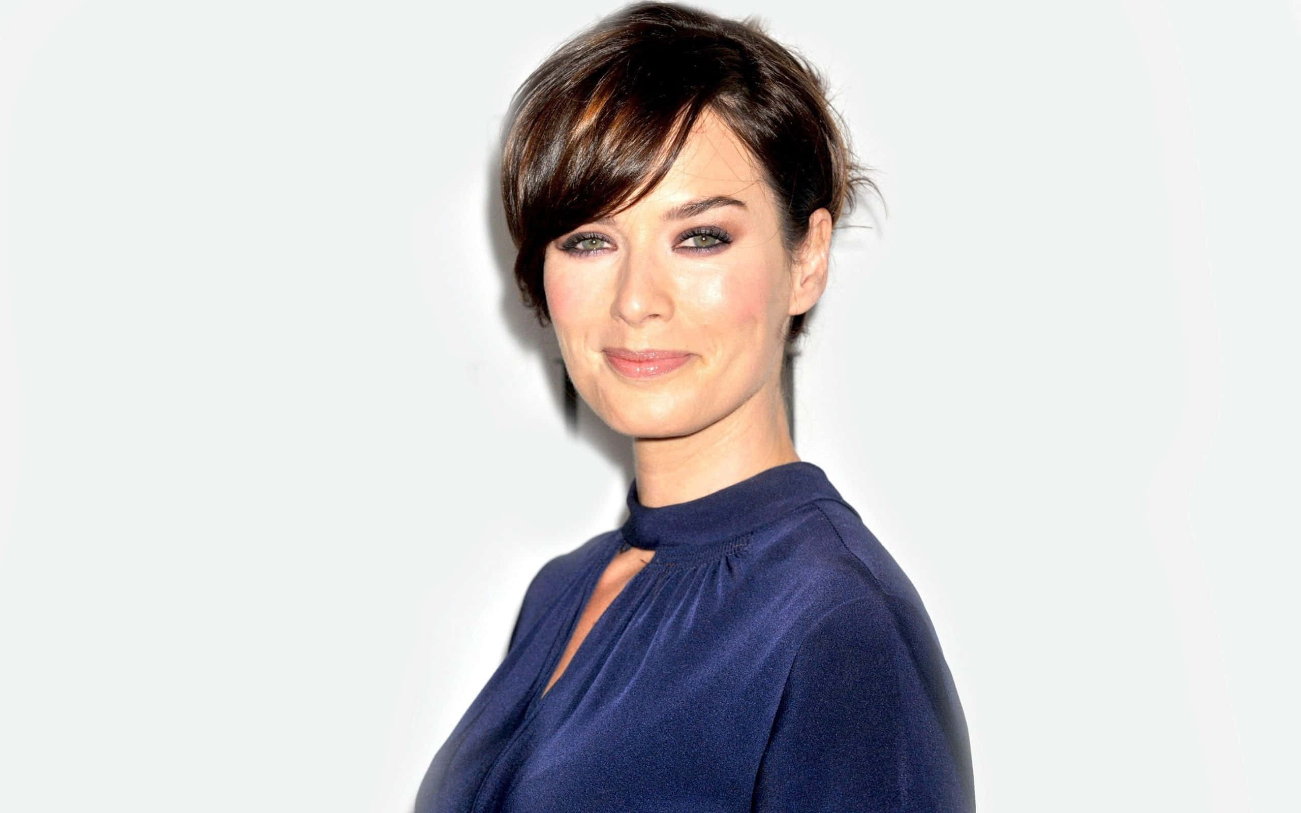 Lena Headey 桌布 壁紙 — 一位短黑髮、身穿海軍藍上衣的女性，在純白背景前帶著溫柔的微笑擺姿勢。