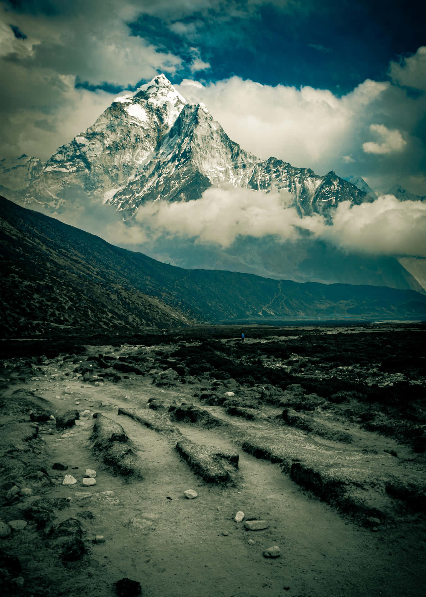 一名徒步旅行者在多雲的天空下沿著岩石小徑走向雄偉的雪山。 — 富士山 壁紙