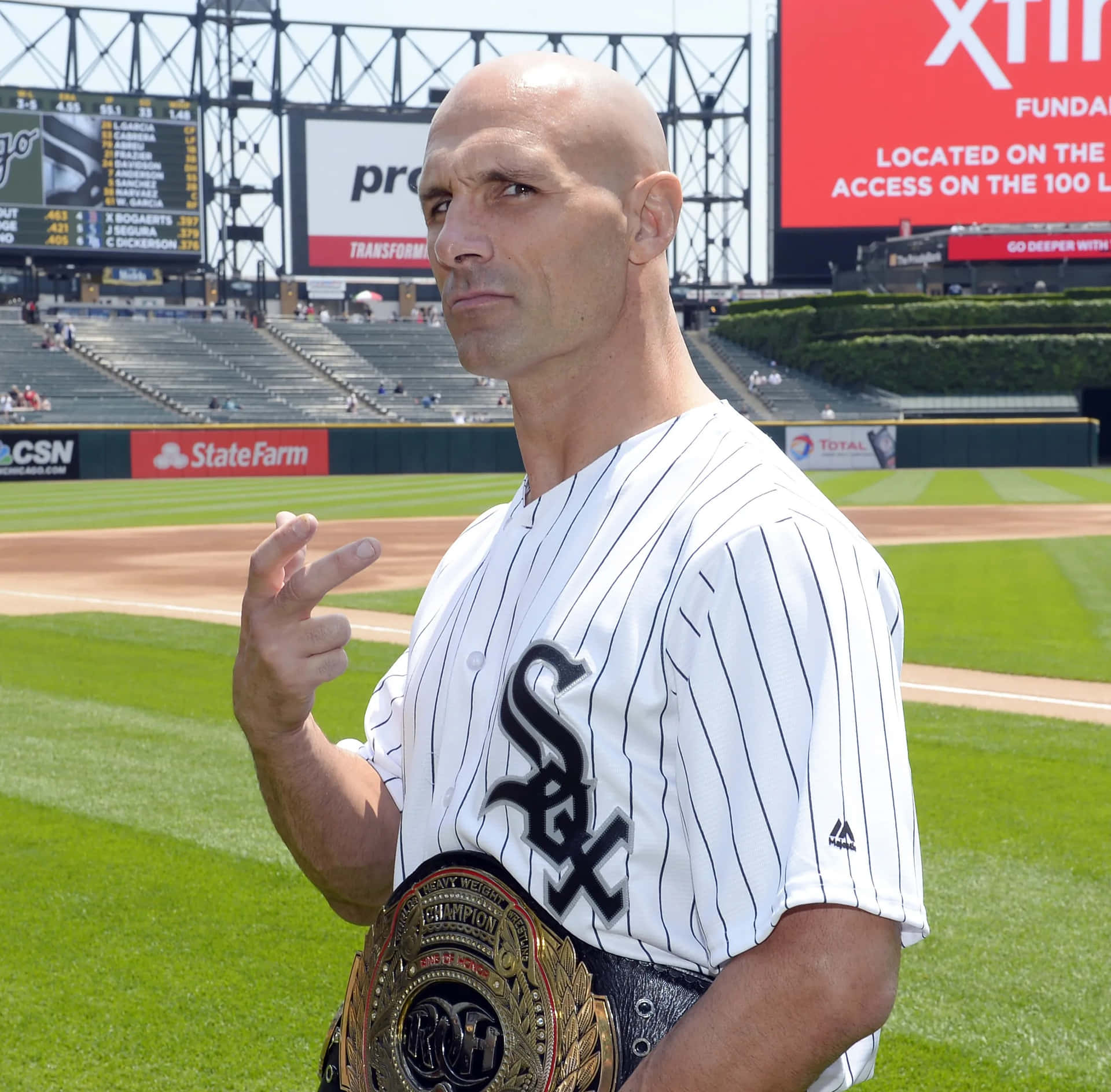  壁紙 — 一位光頭棒球運動員身穿白色細條紋Sox球衣，站在陽光明媚的球場上，手持冠軍腰帶，表情嚴肅地指著。