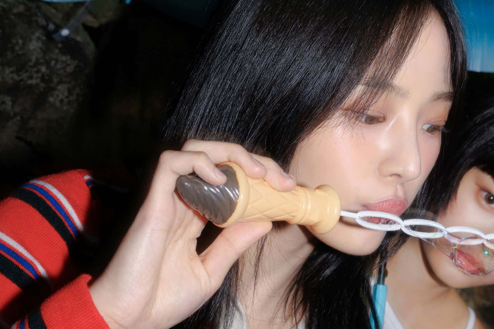  壁紙 — 一位黑髮年輕女子將米色泡泡棒放在唇邊，在昏暗的室內環境中吹泡泡。