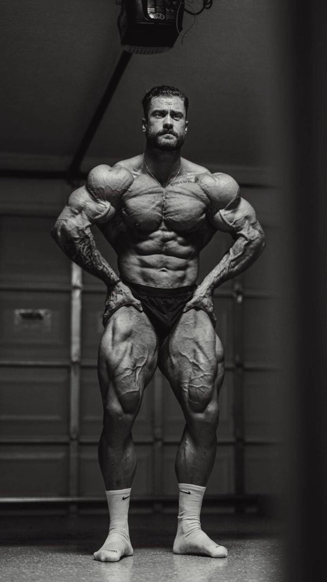 一位肌肉發達的男子在健身房中擺姿勢，擁有清晰的肌肉和紋身。 — Chris Bumstead 壁紙