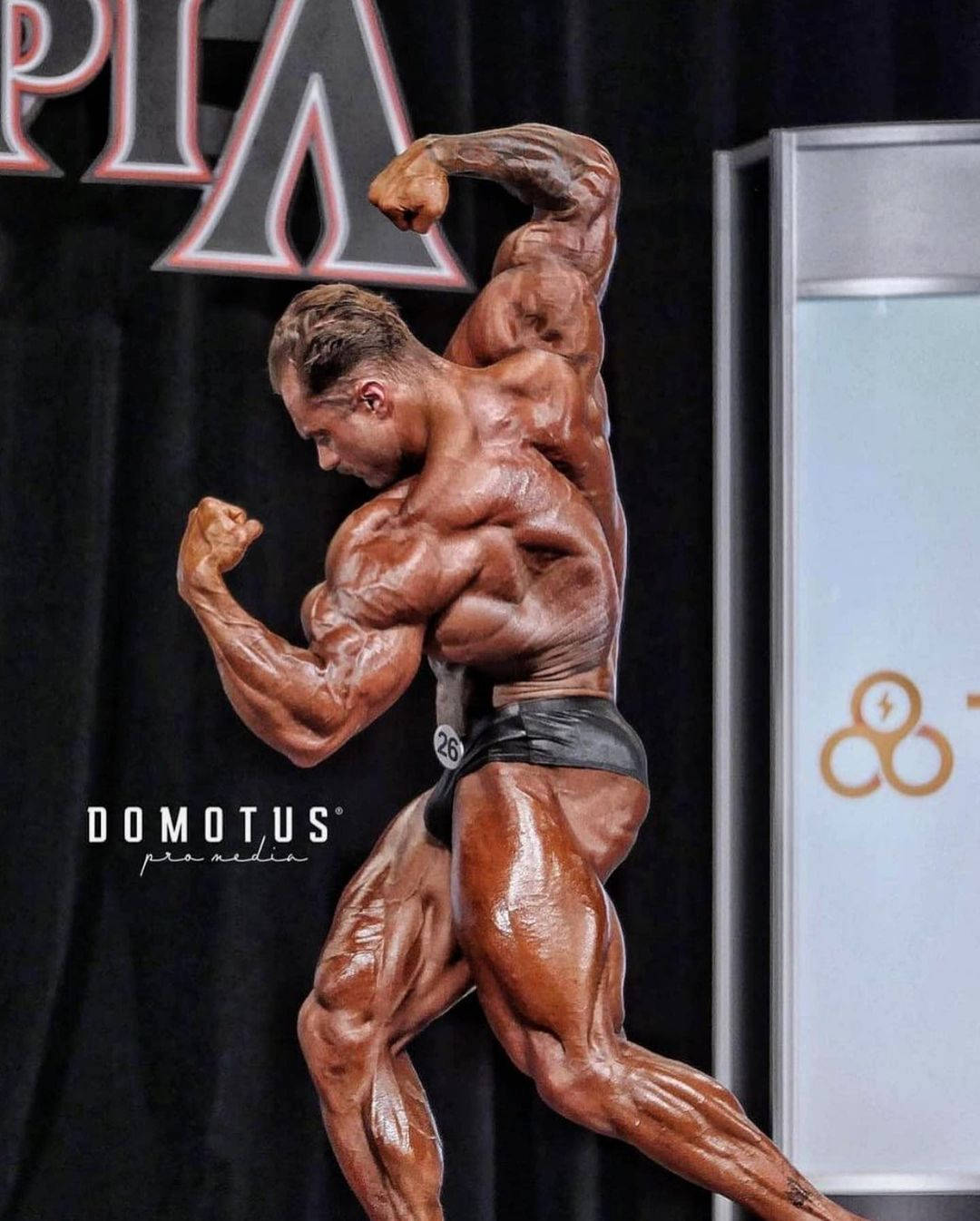 比賽中的健美運動員在舞台上擺出姿勢，肌肉清晰，皮膚閃亮。 — Chris Bumstead 壁紙
