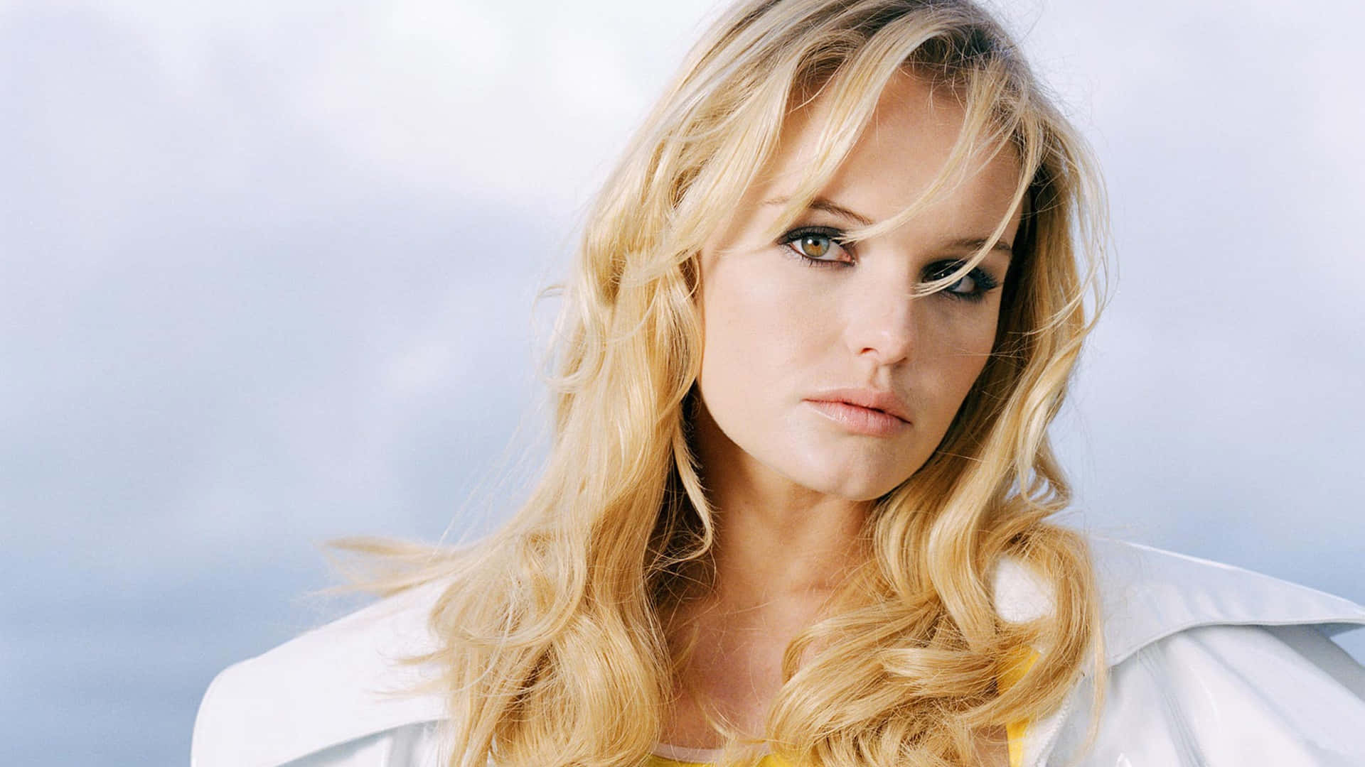 Kate Bosworth 桌布 壁紙 — 一位金髮波浪長髮的女性，在柔和的藍天背景下凝視著。