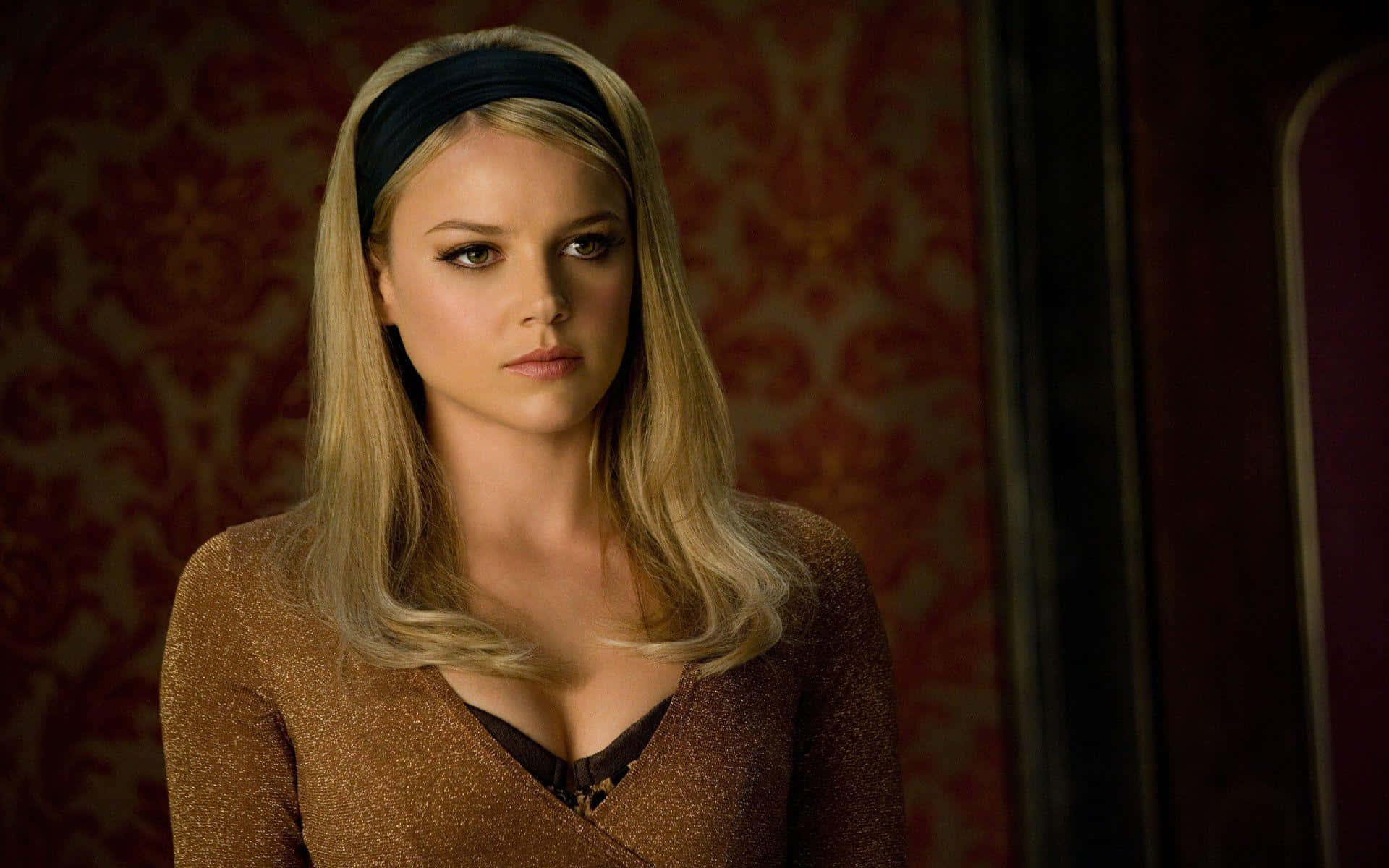 Abbie Cornish 桌布 壁紙 — 一位金髮戴黑色頭帶的女子，在濃郁的紅色錦緞壁紙背景下凝視著。