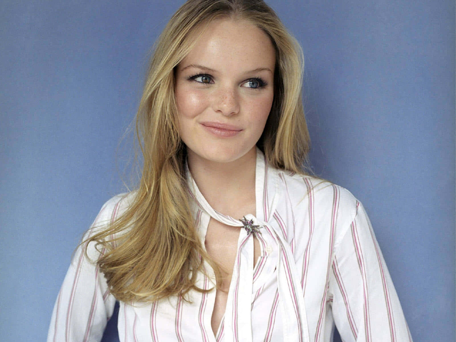 Kate Bosworth 桌布 壁紙 — 一位金髮雀斑的年輕女性，穿著白色條紋襯衫，在純藍色背景前溫柔微笑。