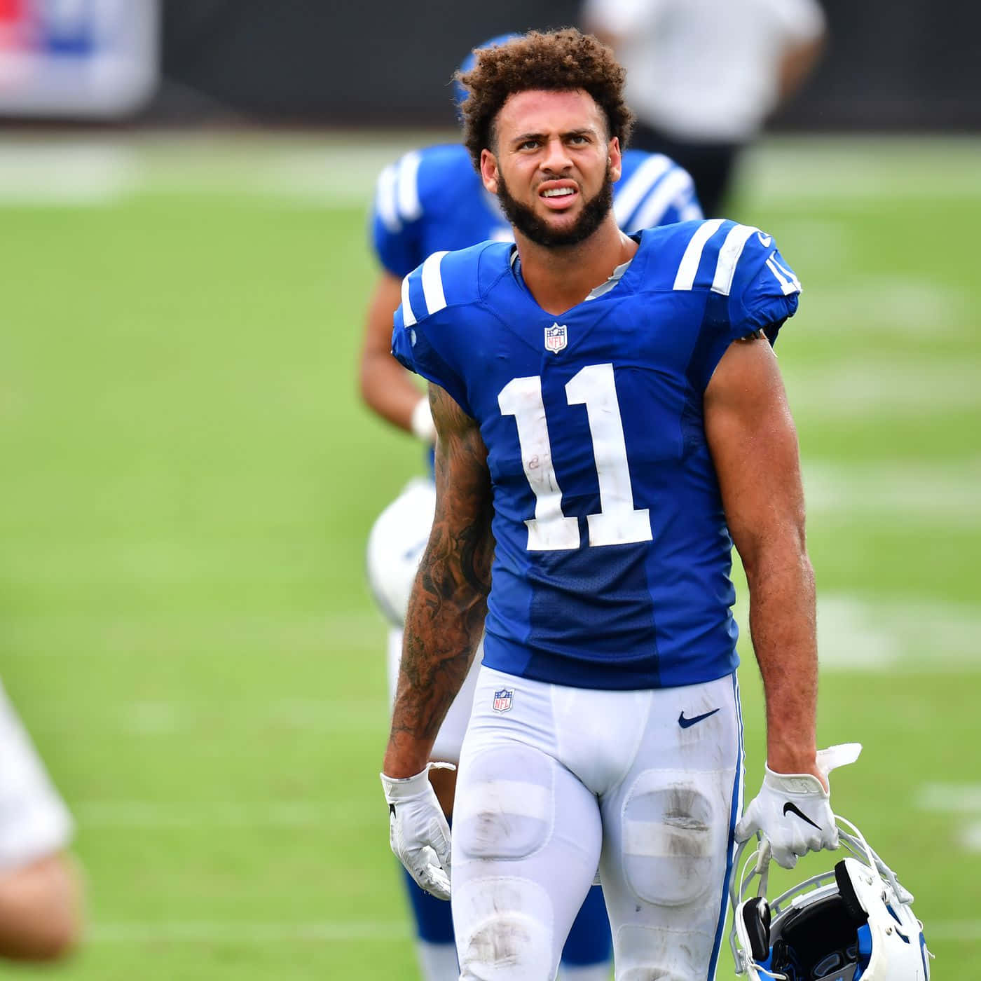  壁紙 — 一位決心堅定的NFL球員身穿藍色球衣，號碼11，手持頭盔走過綠色球場。