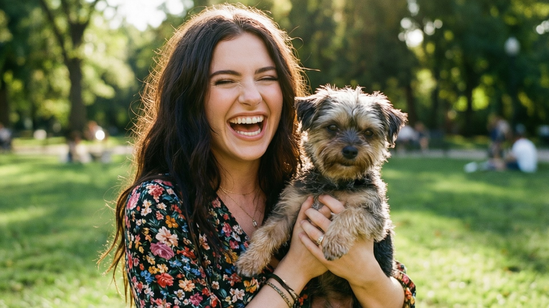 Puppy Love 壁紙 — 一位快樂的女人在陽光明媚的公園裡，綠草和樹木間，抱著一隻毛茸茸的小狗大笑。