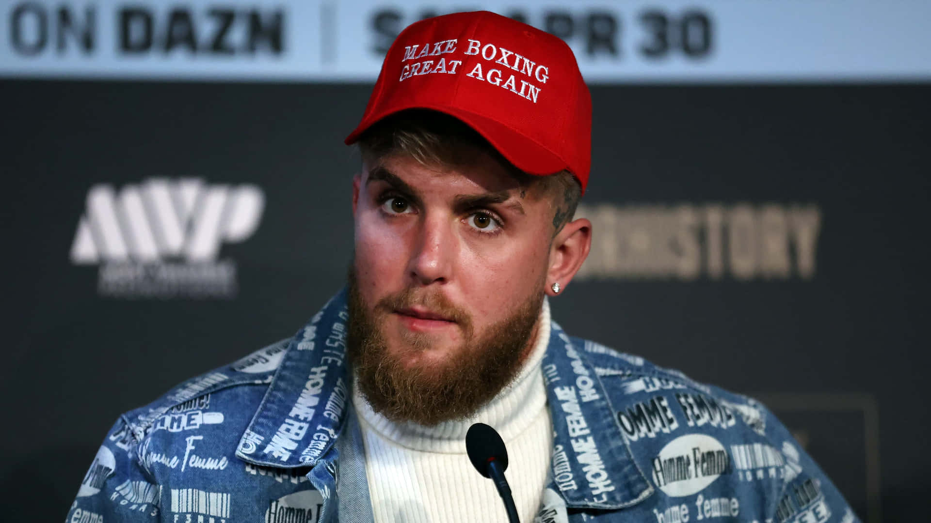 壁紙 — 一位留鬍鬚的男子戴著紅色「Make Boxing Great Again」帽子和穿著品牌牛仔外套在記者會上發言。