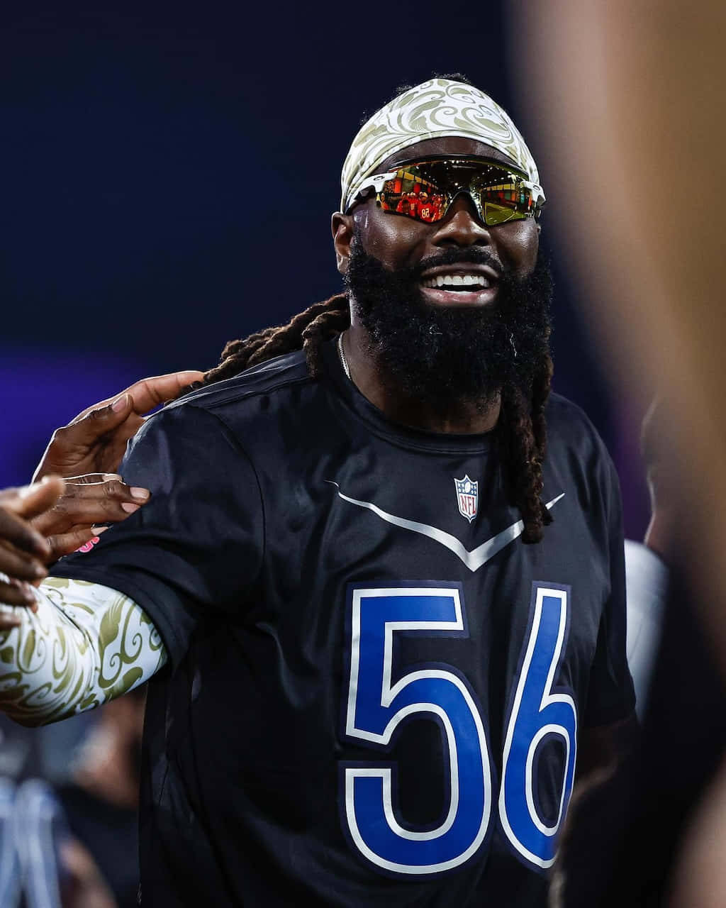  壁紙 — 一位留鬍子、戴圖案頭帶的NFL球員，身穿56號球衣，在體育場燈光下微笑慶祝。