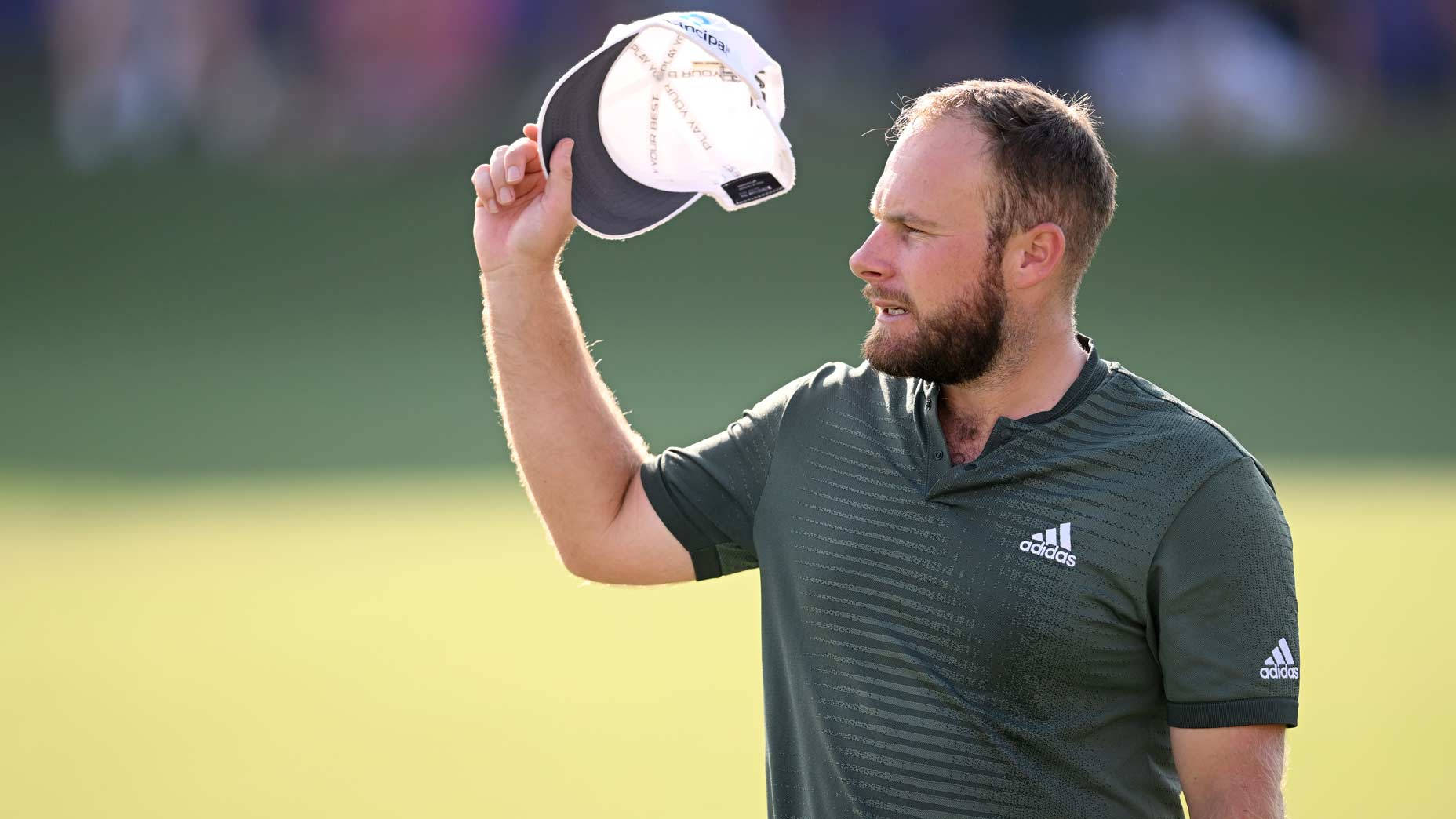 Tyrrell Hatton 桌布 壁紙 — 一位留鬍子的高爾夫球手身穿綠色adidas襯衫，在陽光明媚的高爾夫球場上向觀眾脫帽致意。