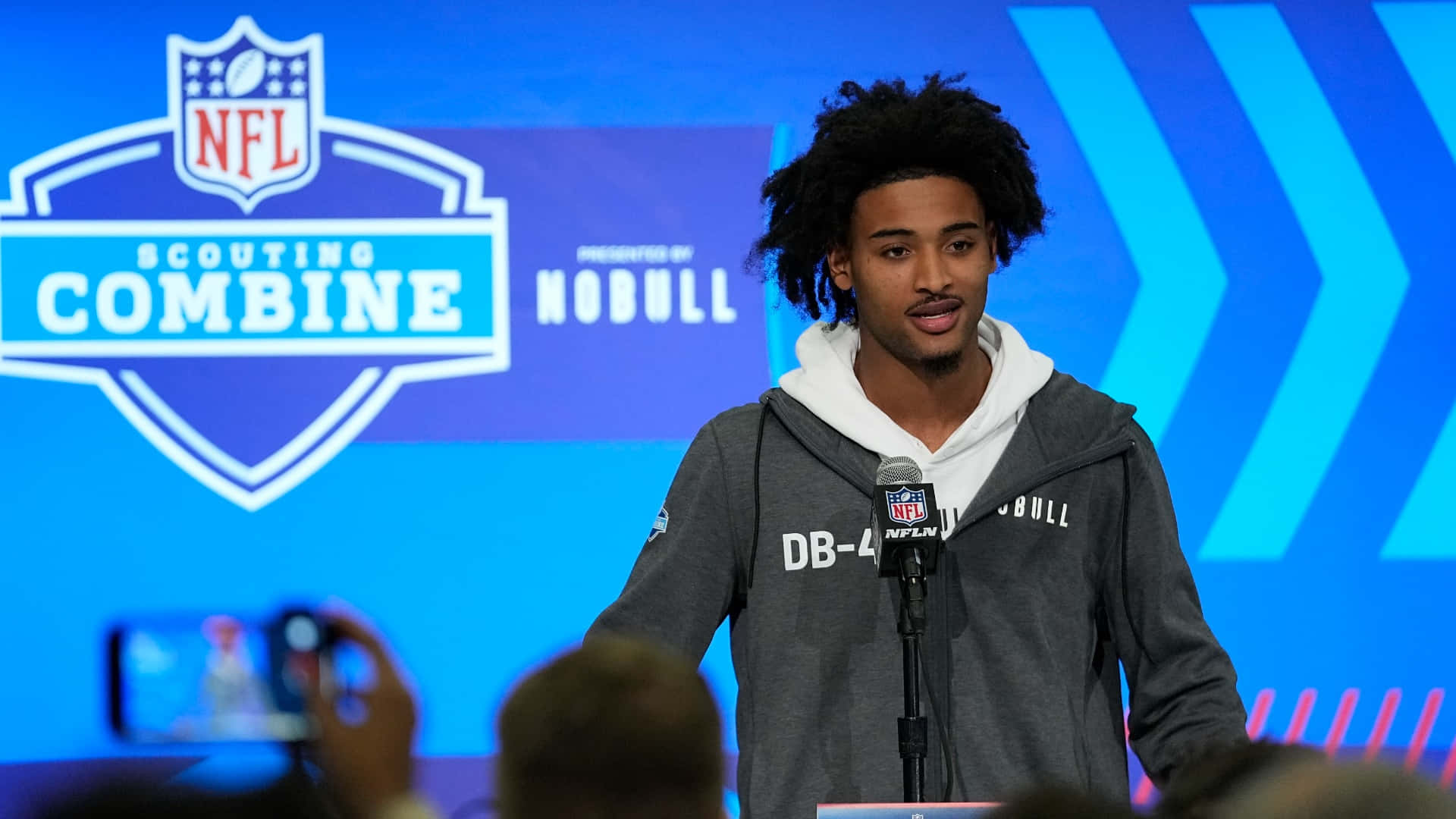  壁紙 — 一位留著辮子的年輕美式足球員在NFL選秀聯合測試活動中對著麥克風發言。