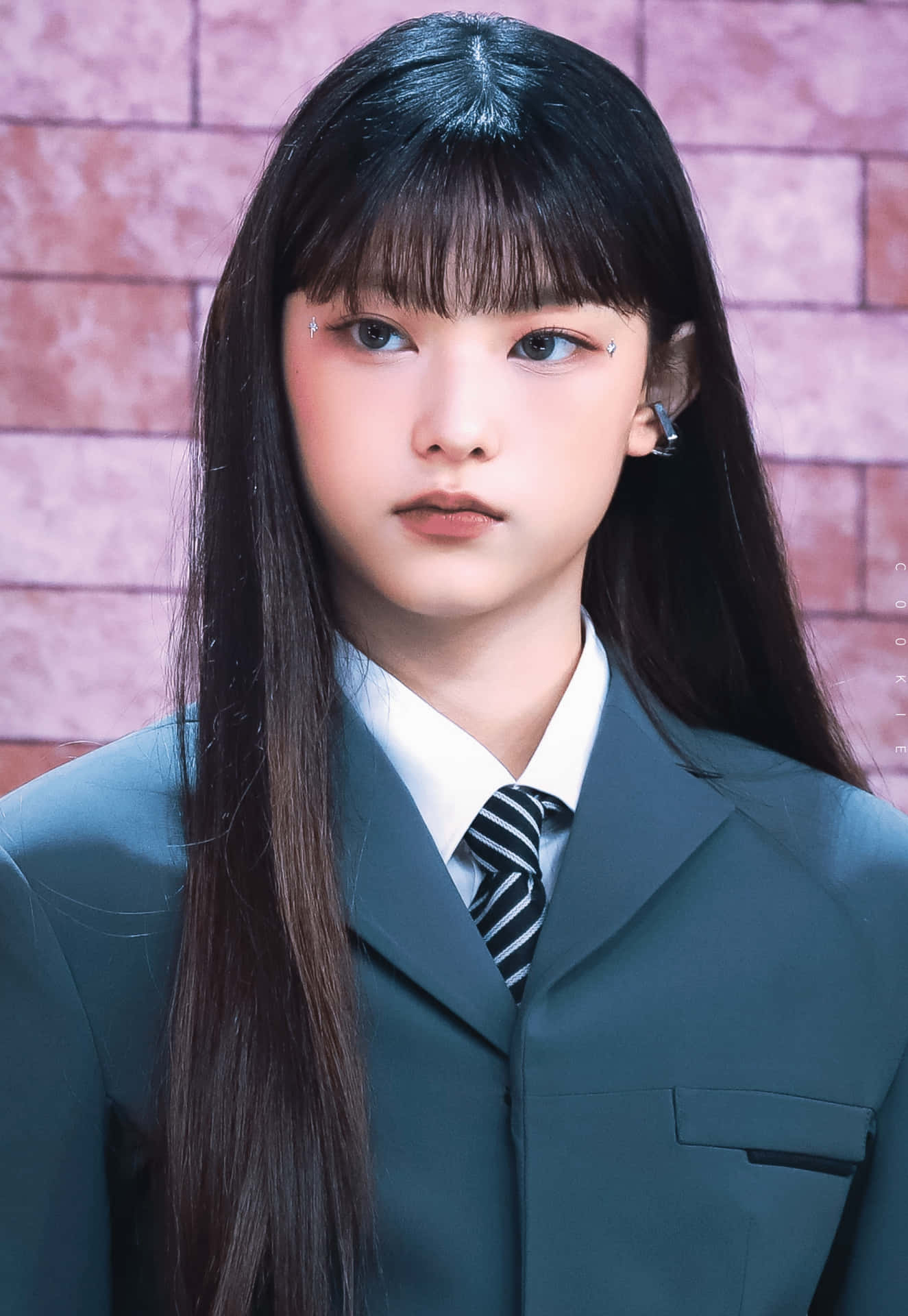  壁紙 — 一位留著長黑髮和瀏海的年輕女性，穿著深綠色校服，背景是粉紅磚牆。